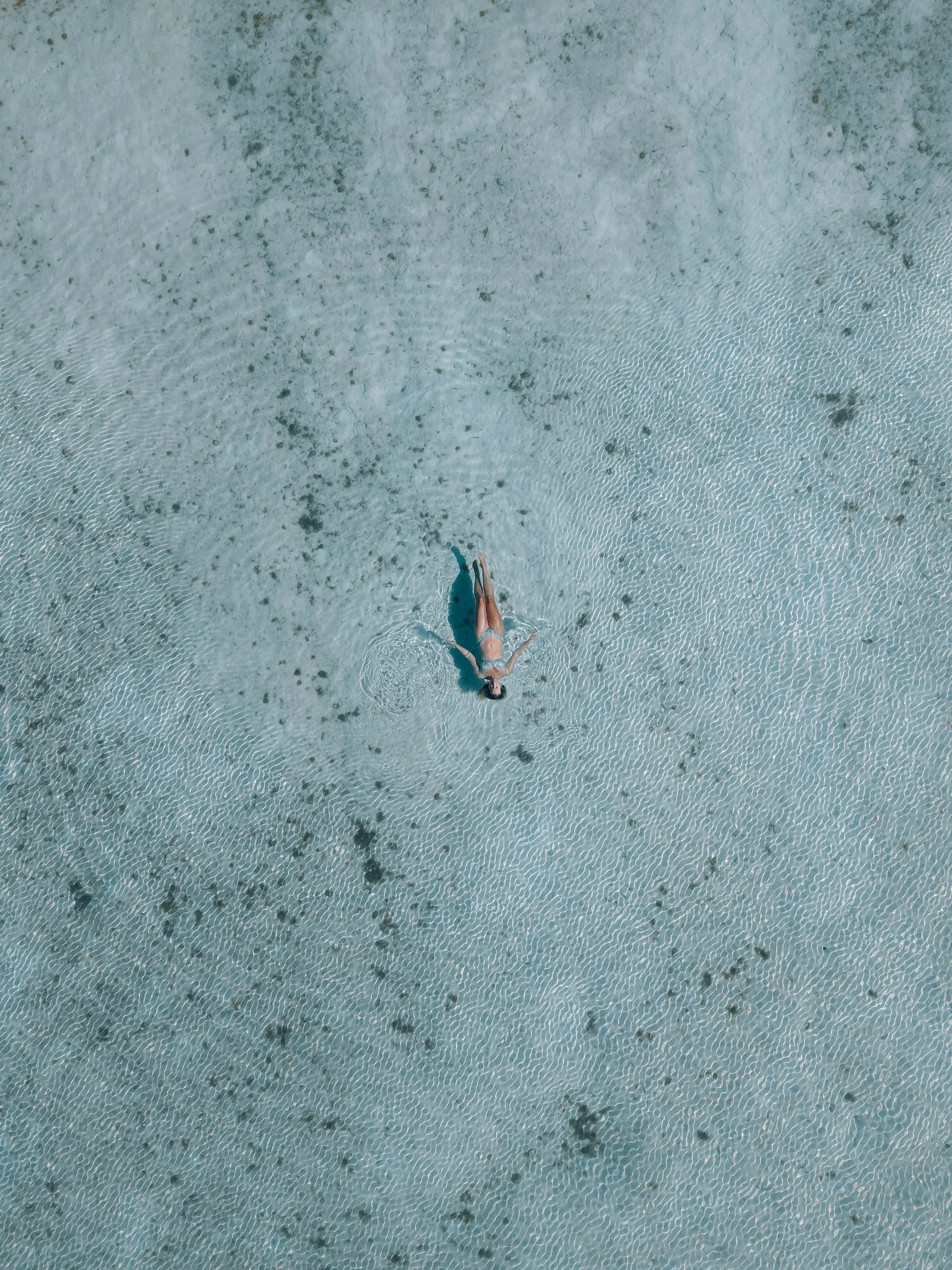 A woman in a bikini lying down in clear shallow water, possibly at a beach or pool.