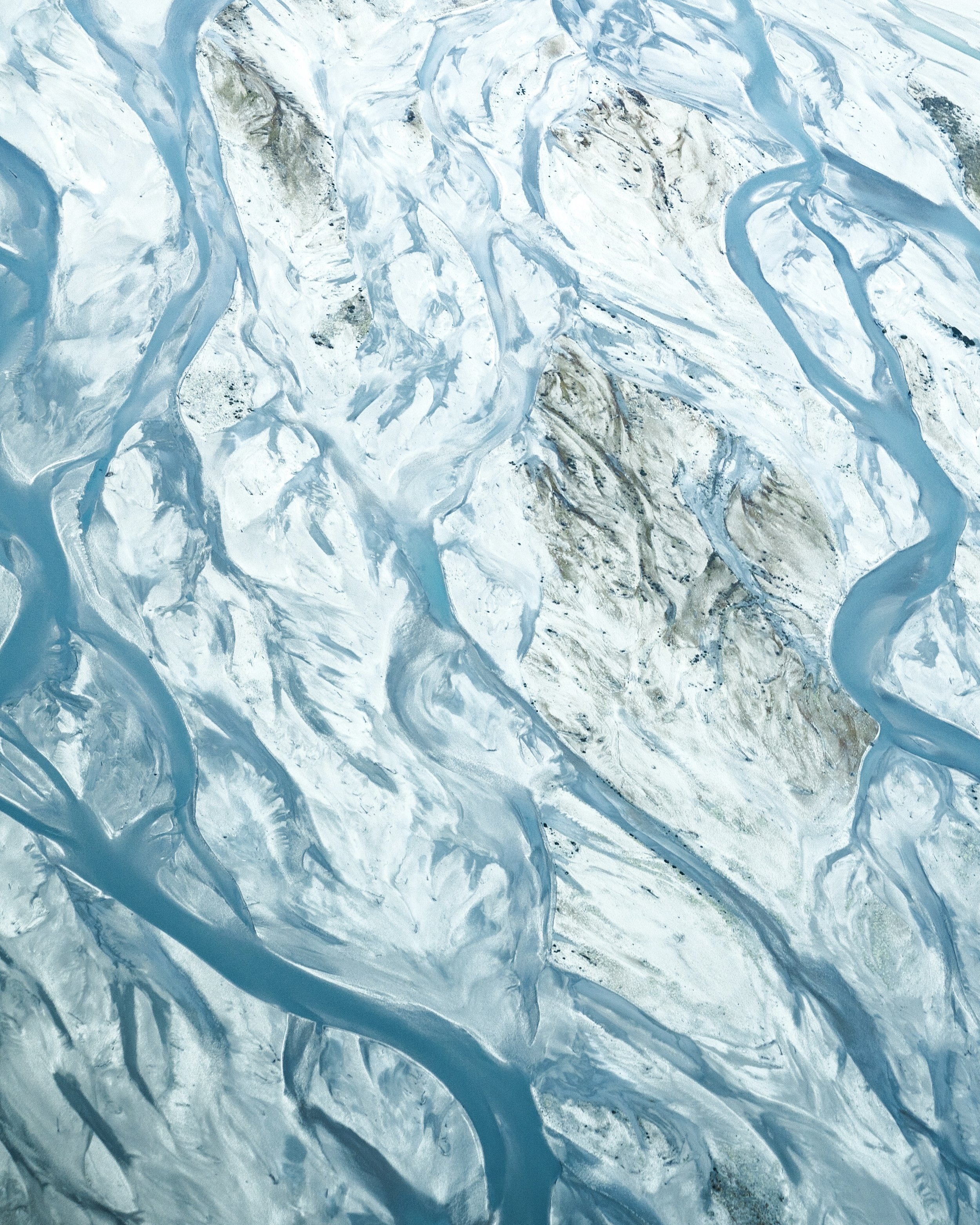 Aerial view of winding rivers and streams flowing through a landscape with snow and ice, possibly a glacial or arctic area.