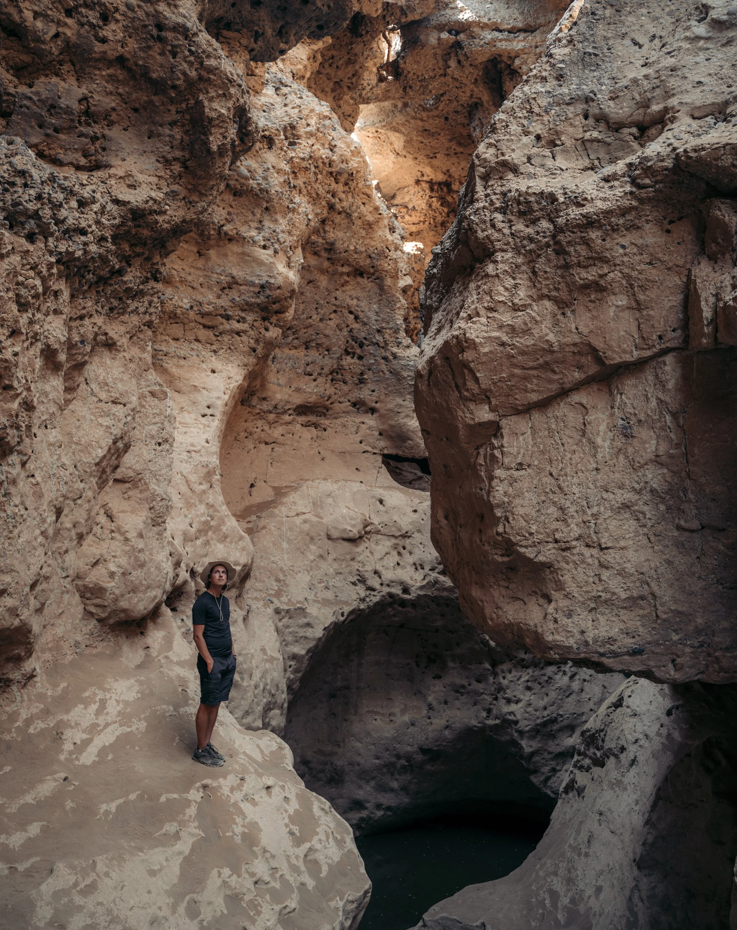 A person standing on rocky terrain inside a canyon with high, textured red and brown rock walls surrounding them.