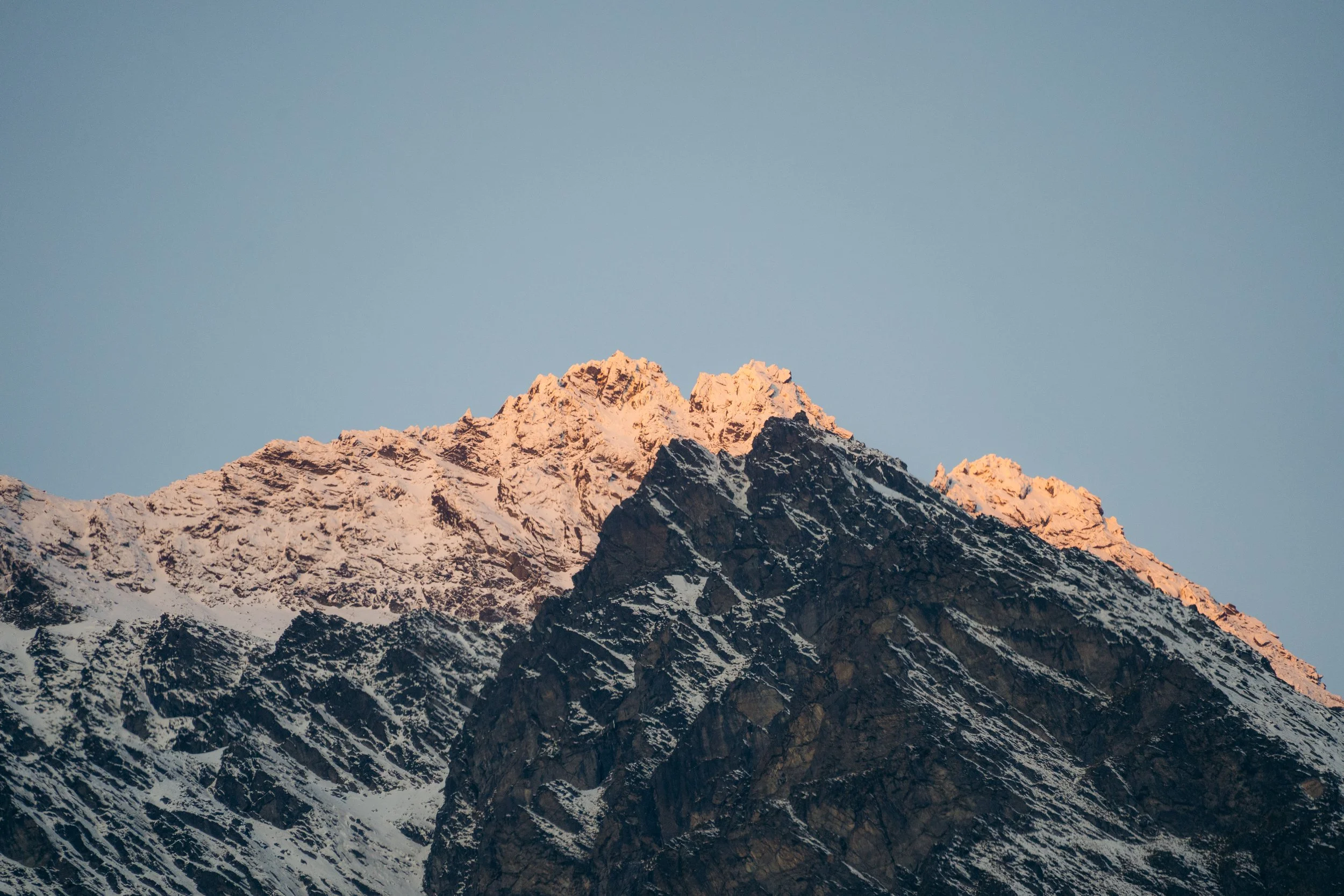 Snow-capped mountain peaks illuminated by sunlight beneath a clear sky.