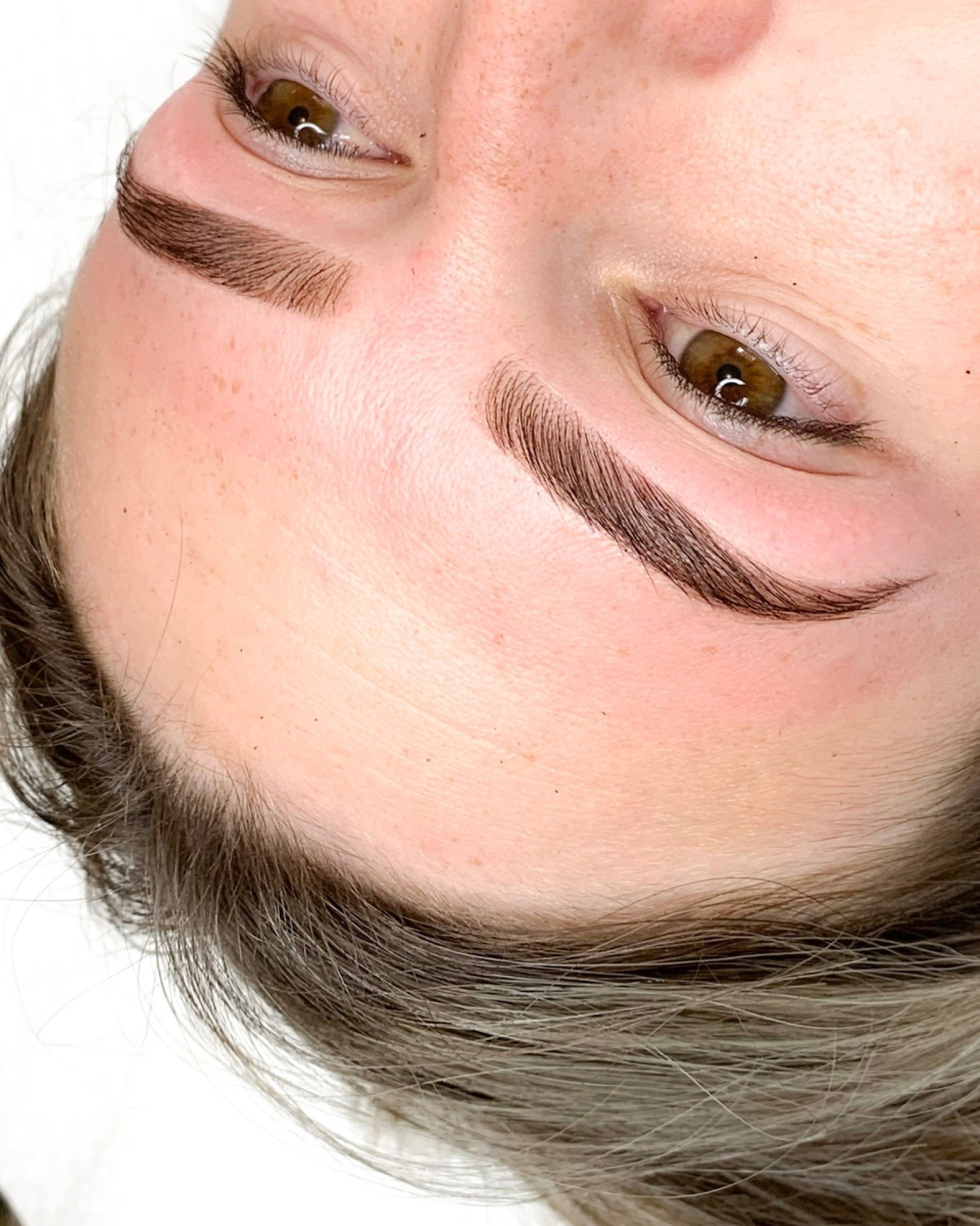 Close-up of a person's face with brown eyes, long eyelashes, and well-shaped eyebrows, showing part of the forehead, nose, and brown hair.