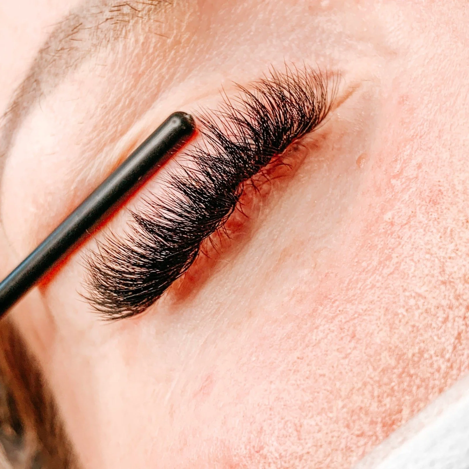 Close-up of a person's closed eye with long, thick, black eyelashes and eyebrow hair visible.