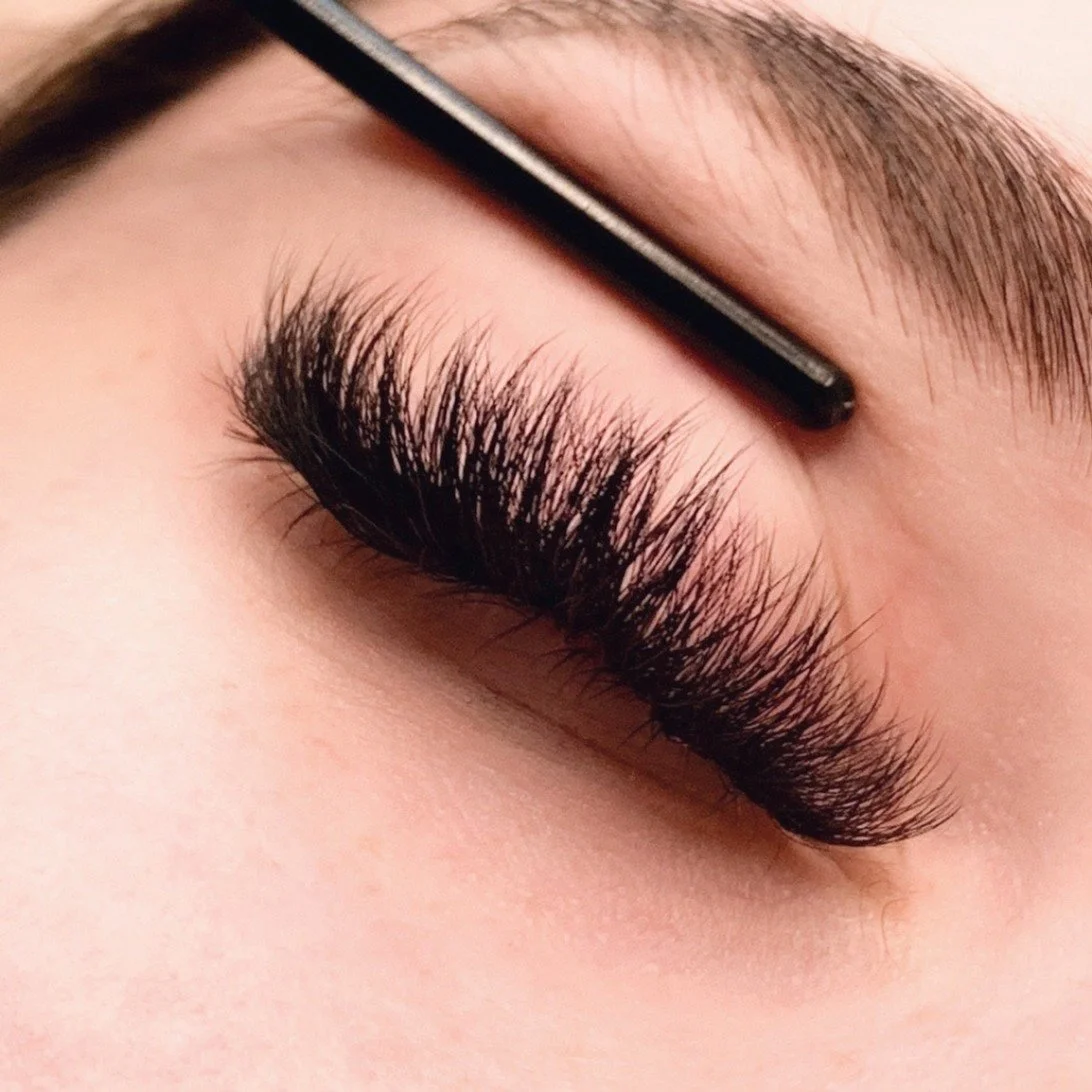 Close-up of a person's closed eye with long, thick, curled eyelashes and well-groomed eyebrow.