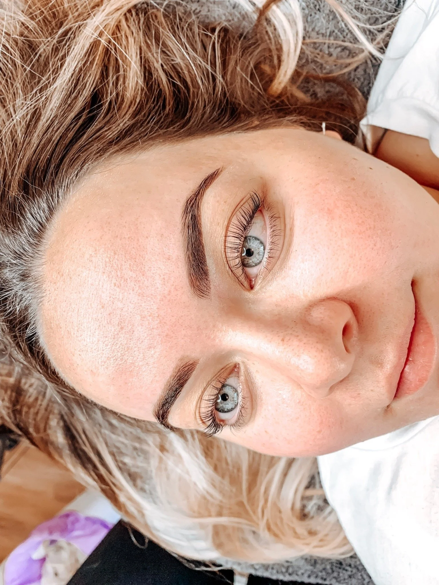 Close-up of a woman's face with blue eyes, curly light brown hair, and light skin, lying down on a surface.