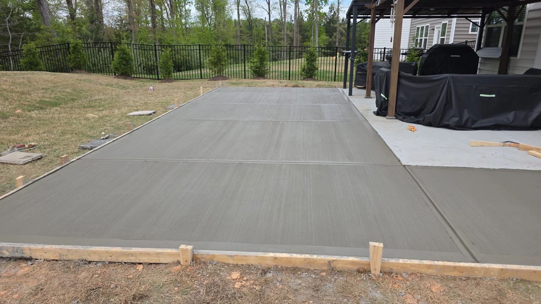 Concrete patio extension for outdoor living in a residential backyard, expanding a small builder-grade slab into a larger usable space. The new poured concrete blends into the existing surface, creating a seamless extension designed for outdoor seati