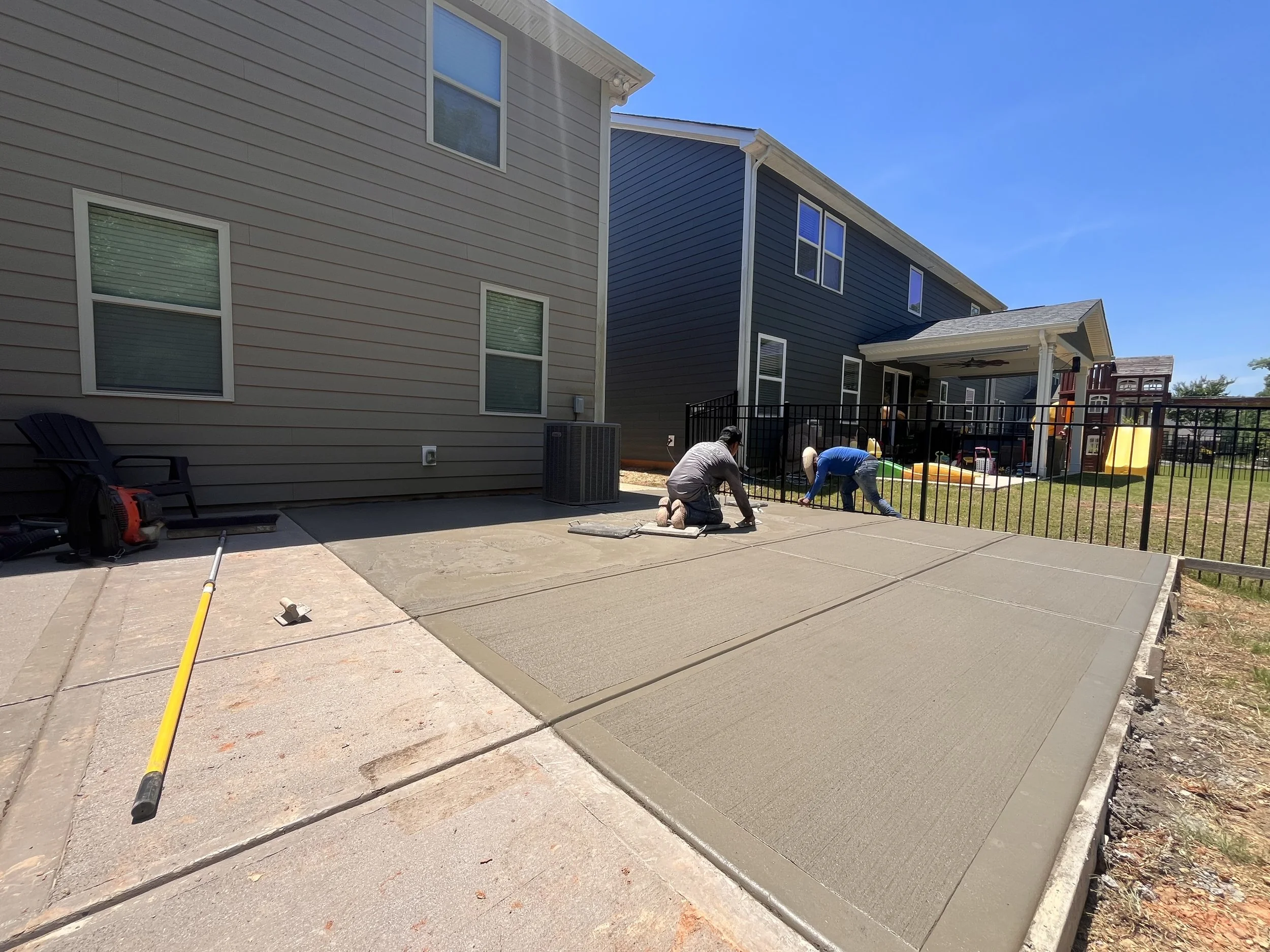 Concrete patio extension for outdoor living in a residential backyard, expanding a small builder-grade slab into a larger usable space. The new poured concrete blends into the existing surface, creating a seamless extension designed for outdoor seati