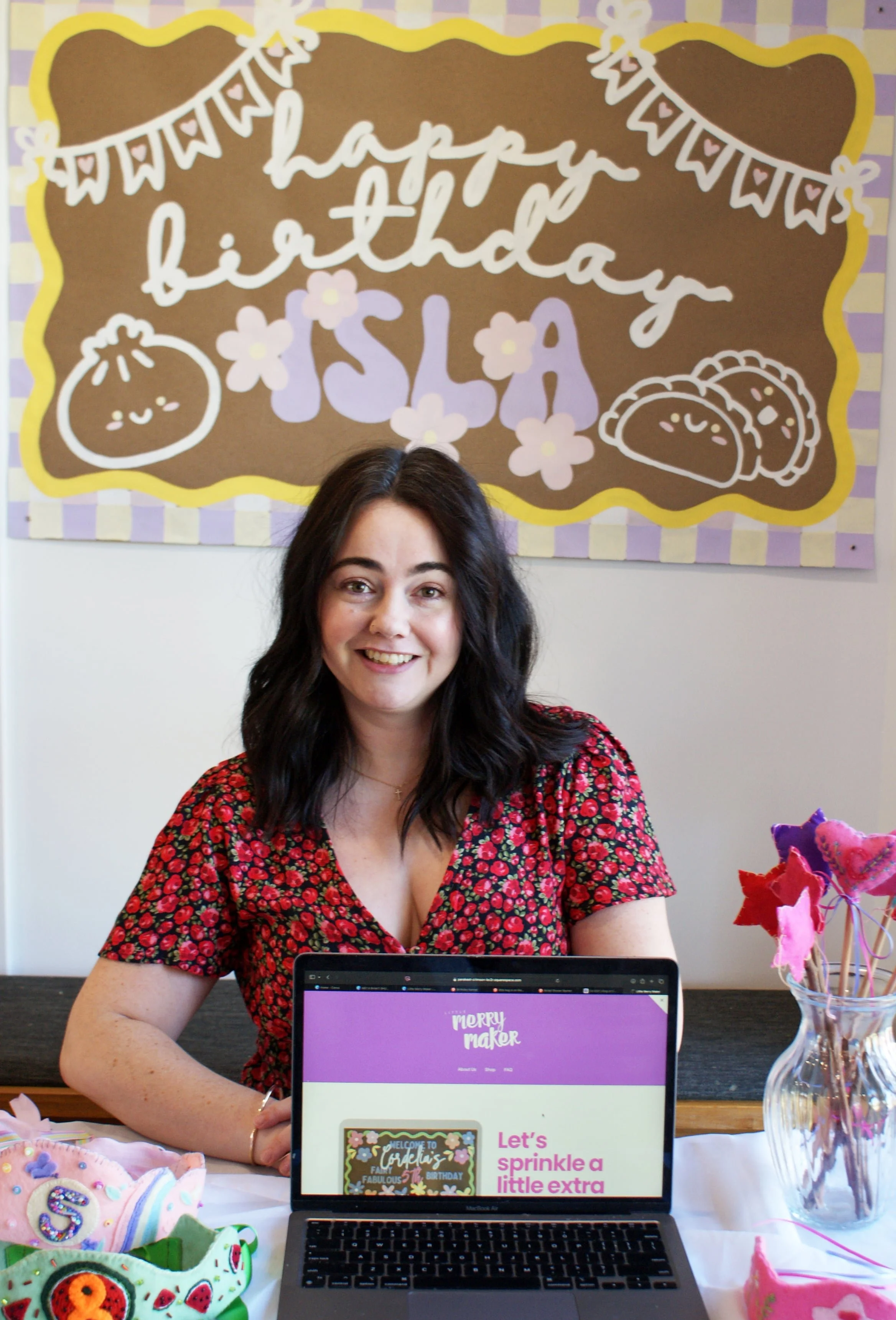 A woman in front of a banner with a laptop, wand, and crown in front of her.