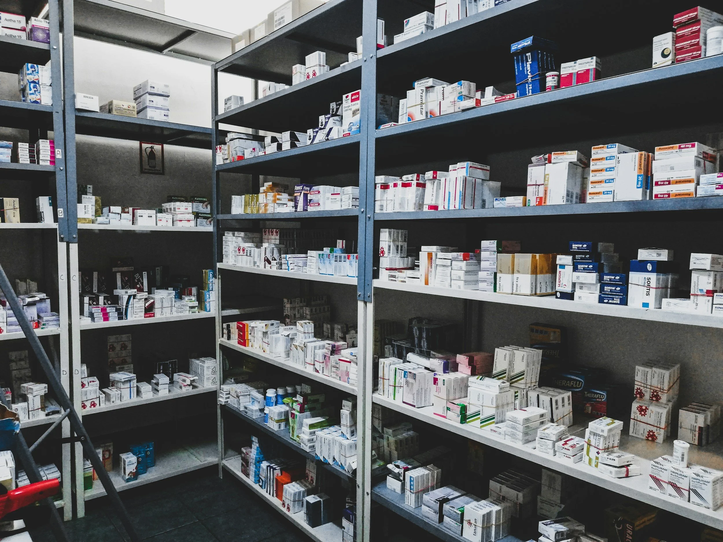 Shelves stocked with various pharmaceutical boxes, inside a pharmacy or storage room.