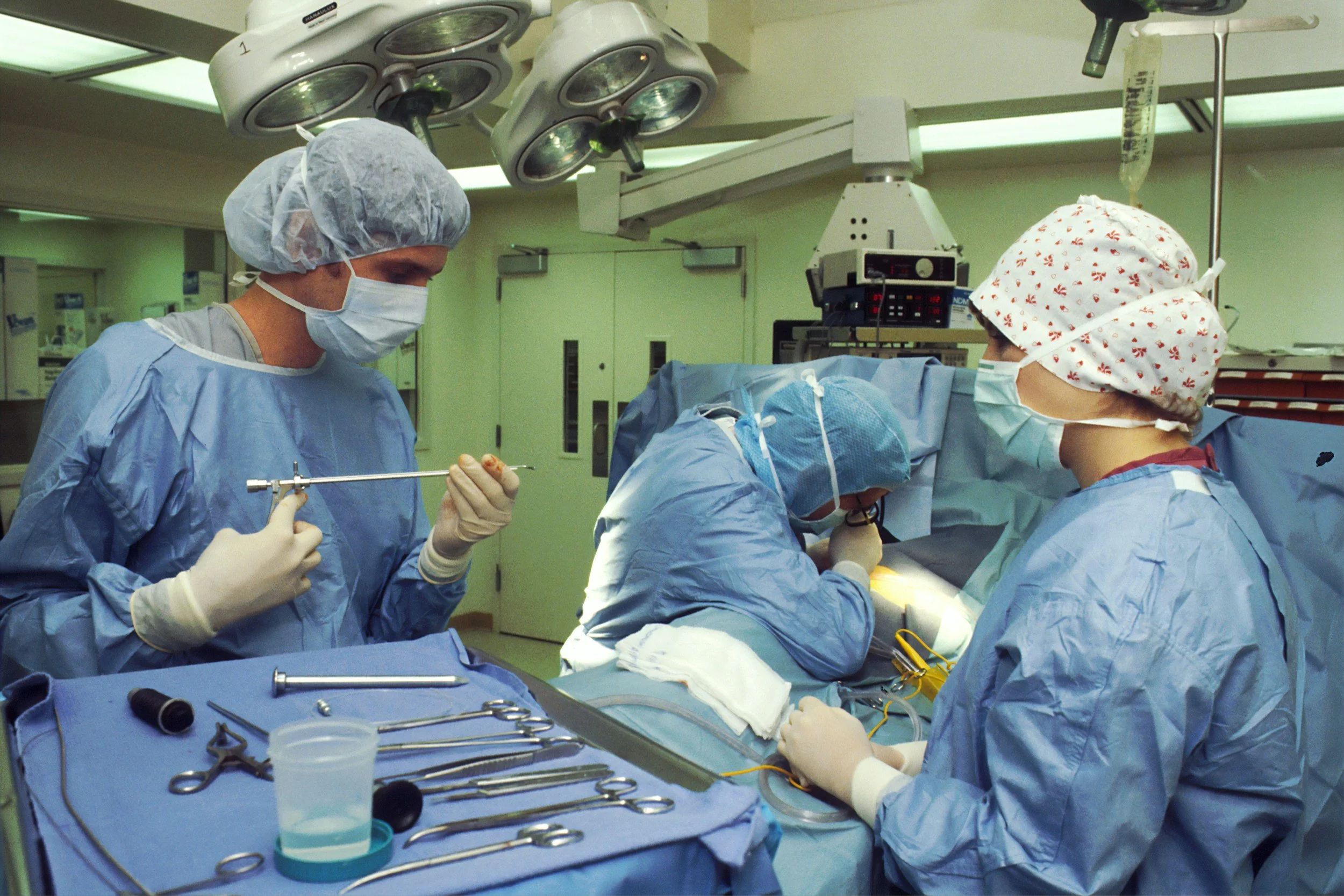 Medical team performing surgery in an operating room, with surgical instruments and equipment visible on a tray.