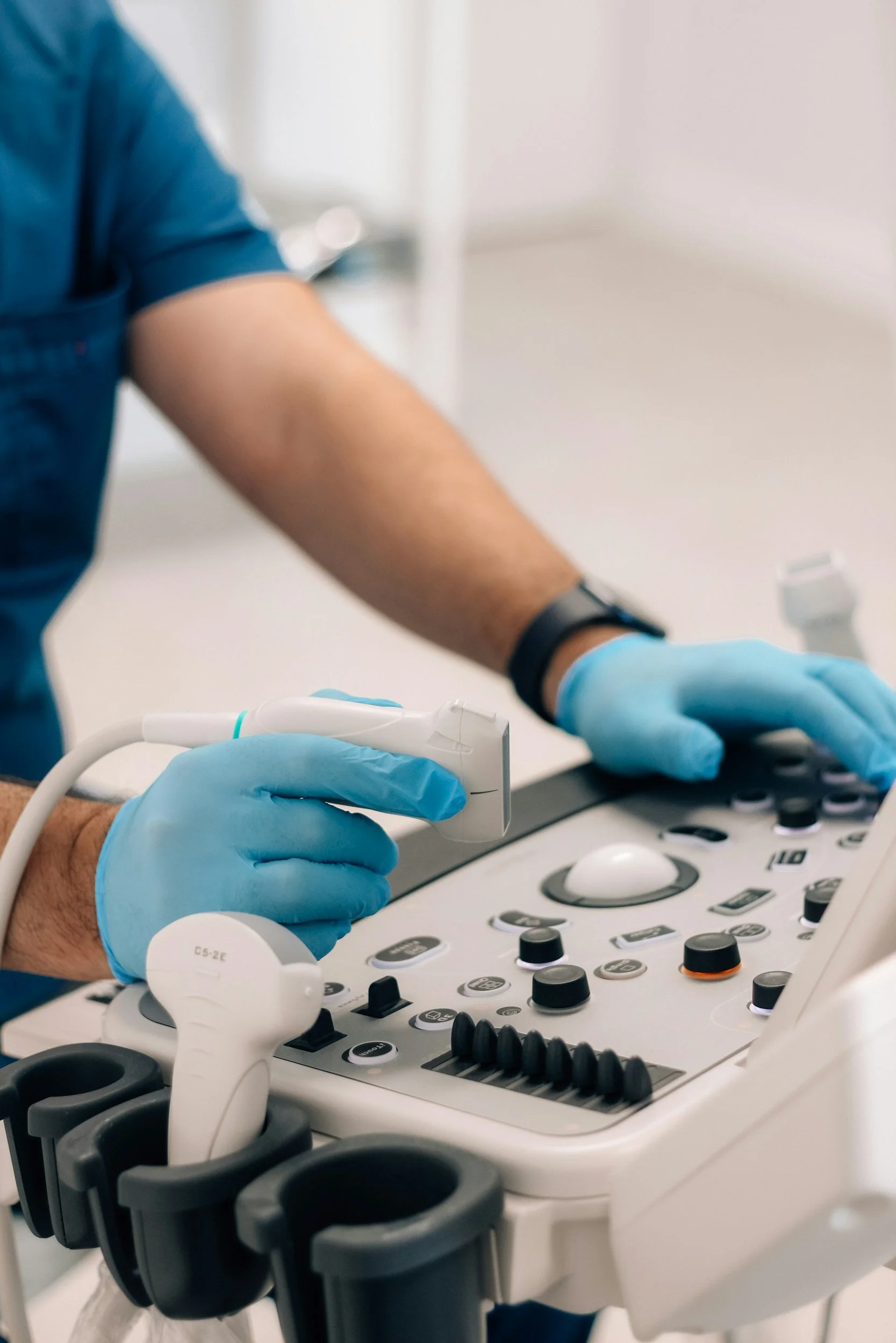 Close-up of a person wearing blue gloves working with medical or laboratory equipment that has various buttons and dials, possibly an ultrasound machine or similar device.