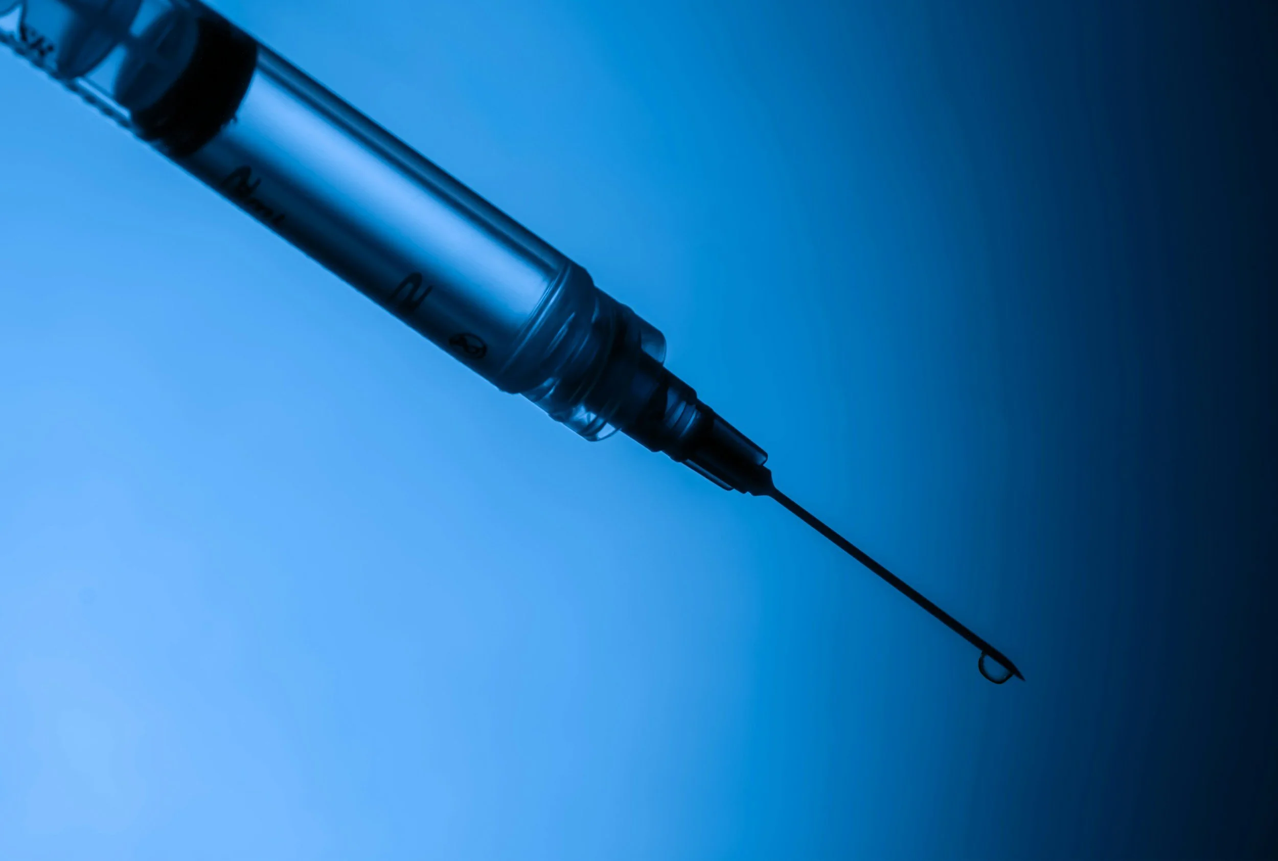 Close-up of a hypodermic syringe with a needle, set against a blue gradient background.