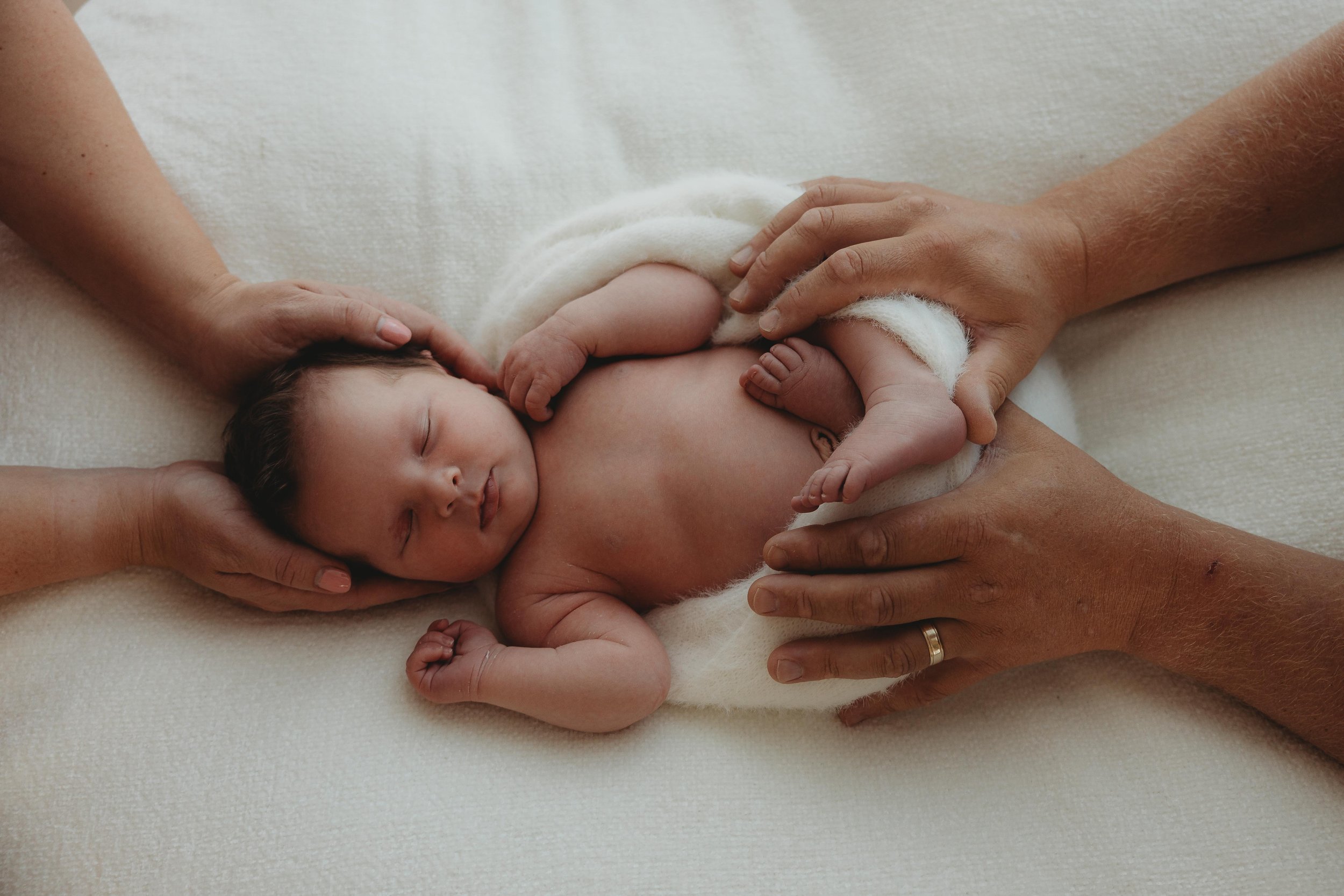 newborn baby being held by parents on head and feet