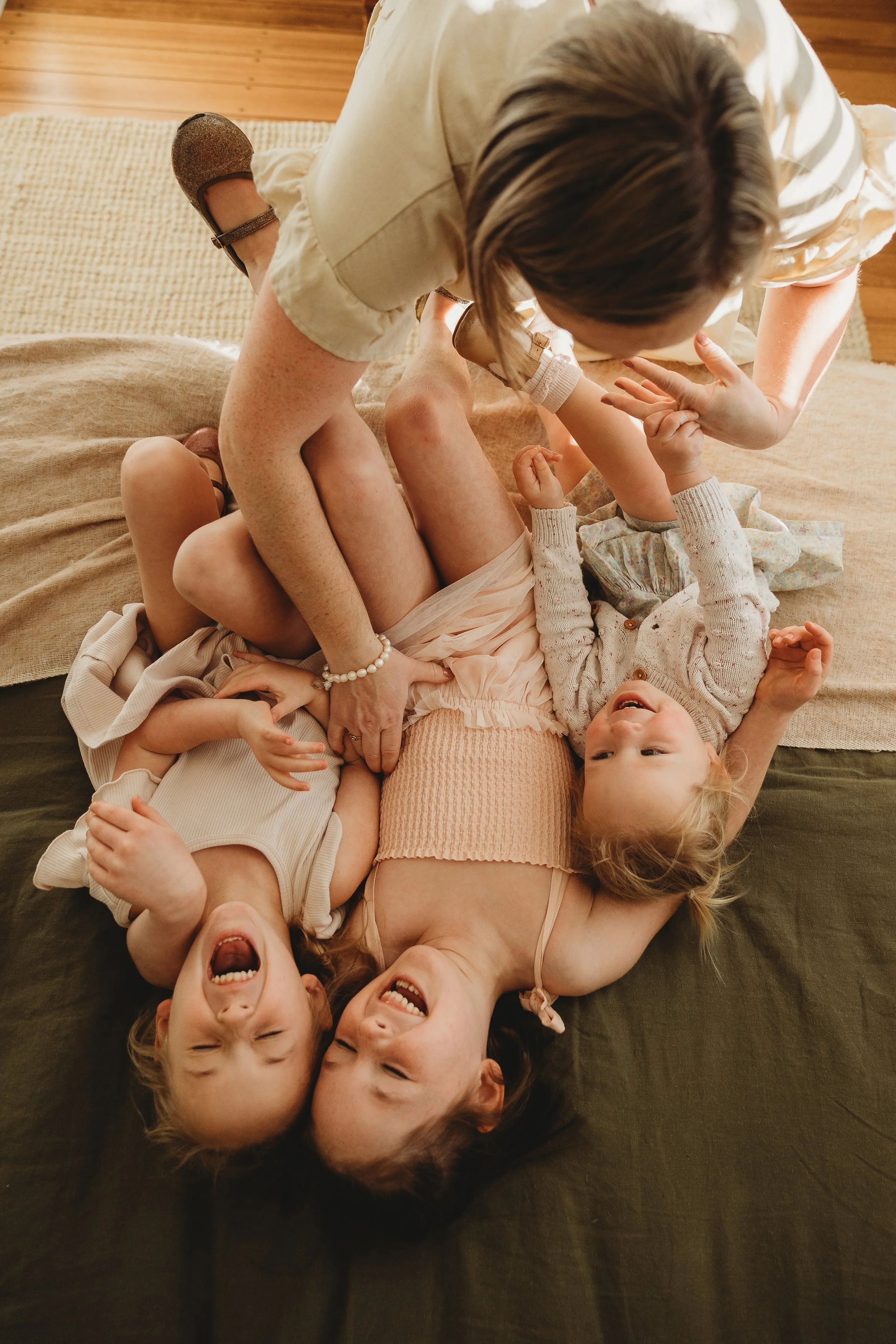 three kids laughing together being ticked by mum