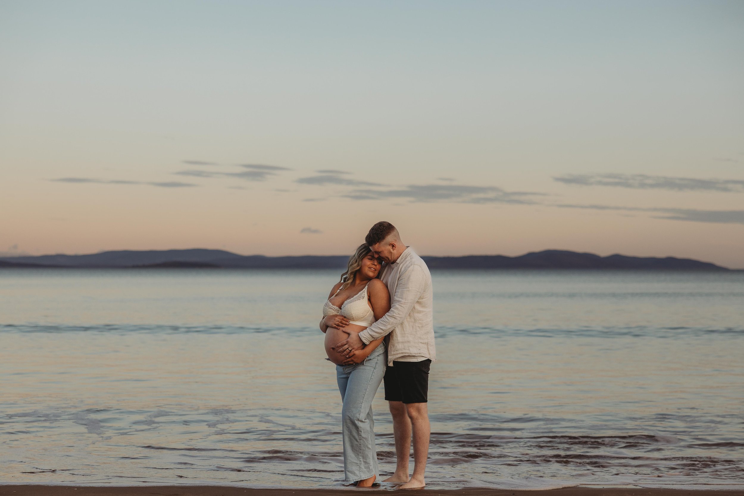Pregnant mum and dad hugging at sunset on the beach