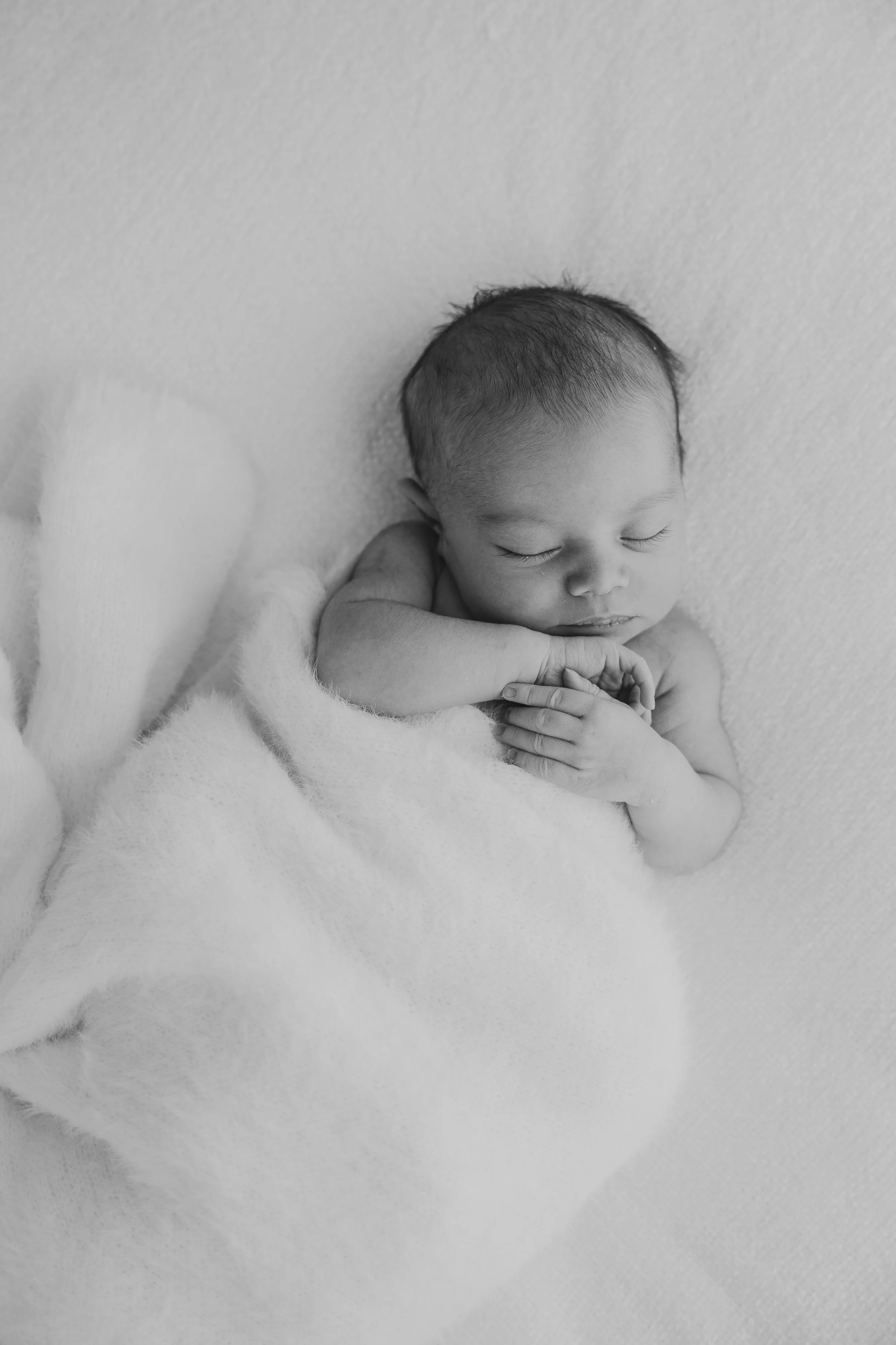 baby in mums arms with face squished in arms and holding mums  thumb 