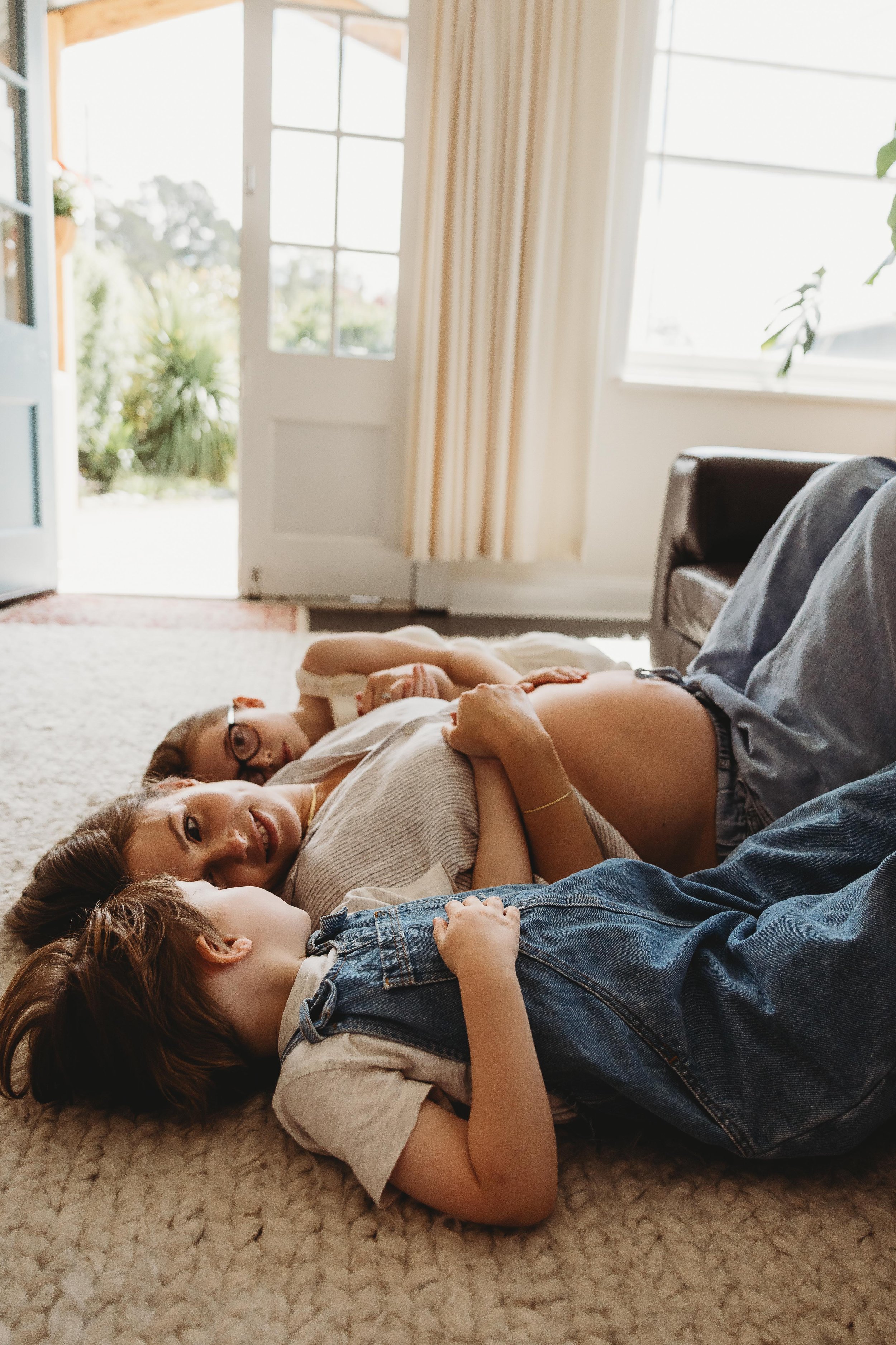 pregnant mum laying on ground with older children laughing