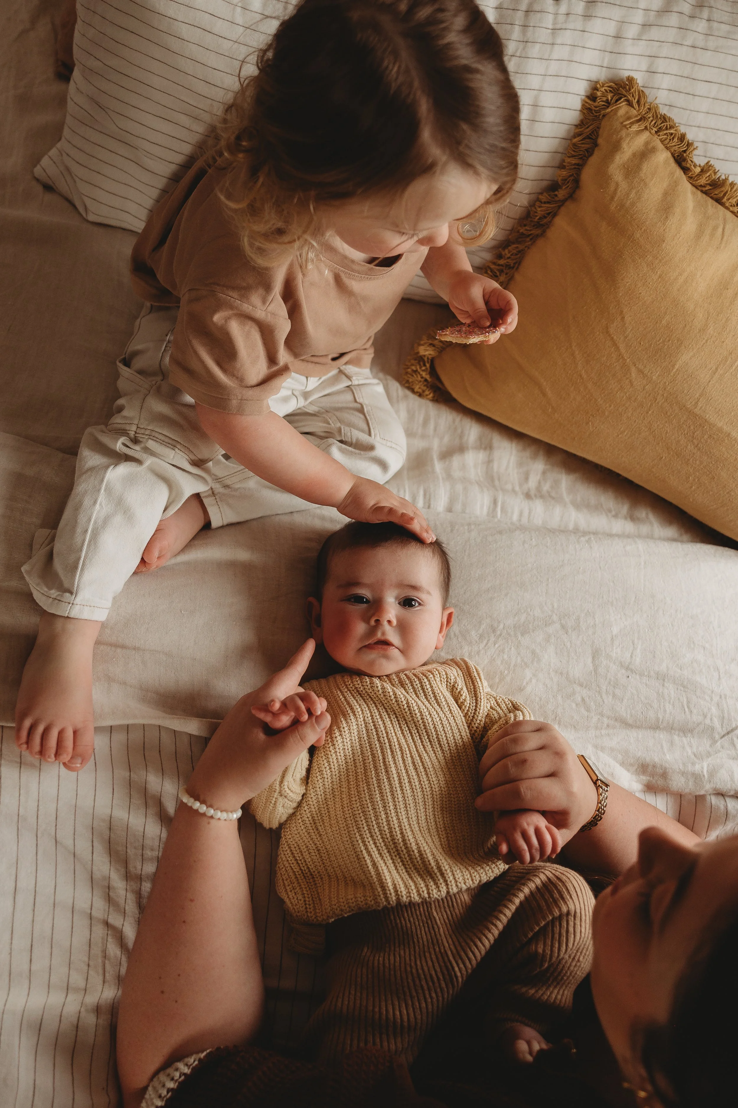 Mum with two young kids on bed tickling baby