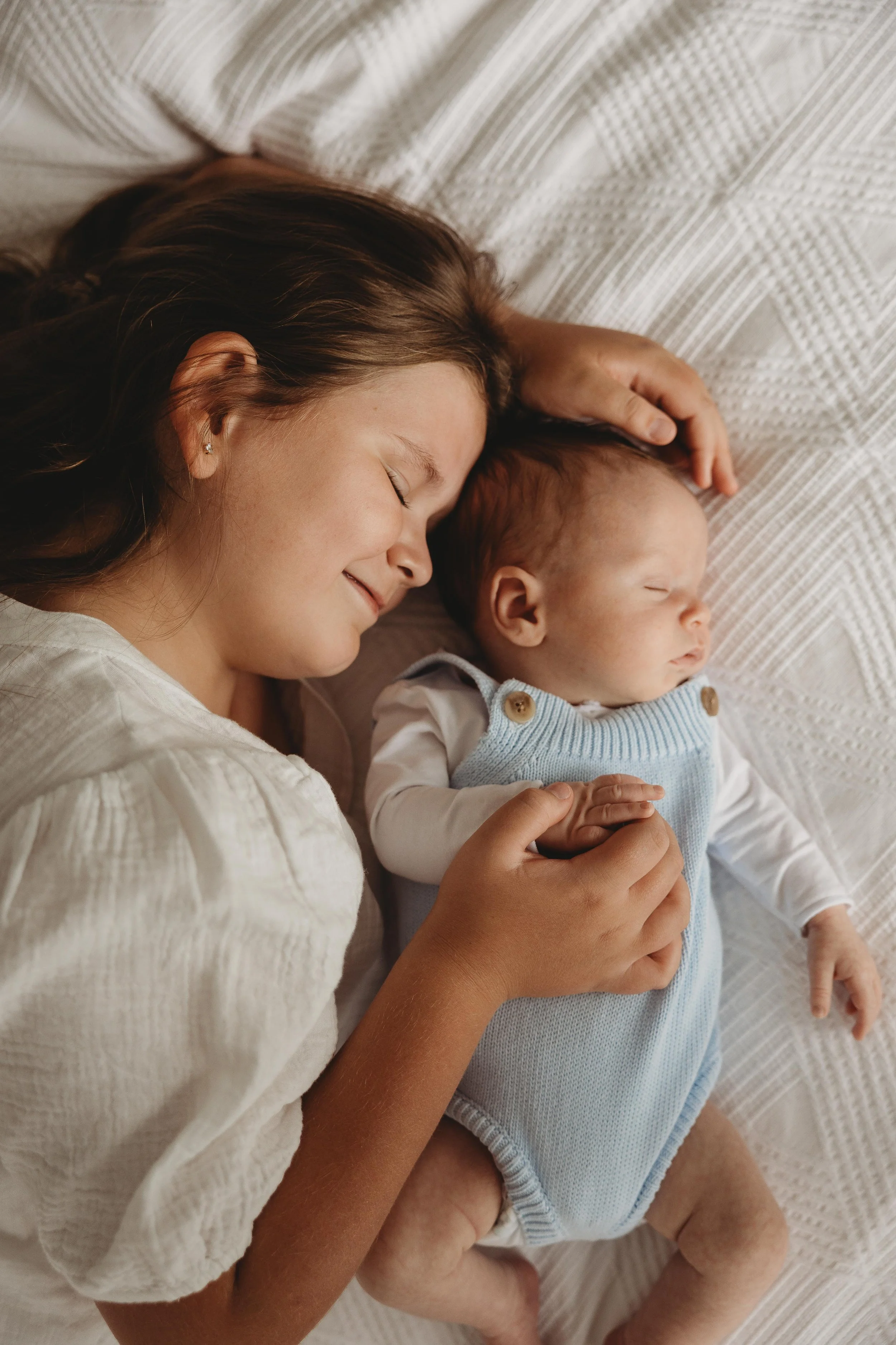 Big sister with newborn baby boy on bed cuddling