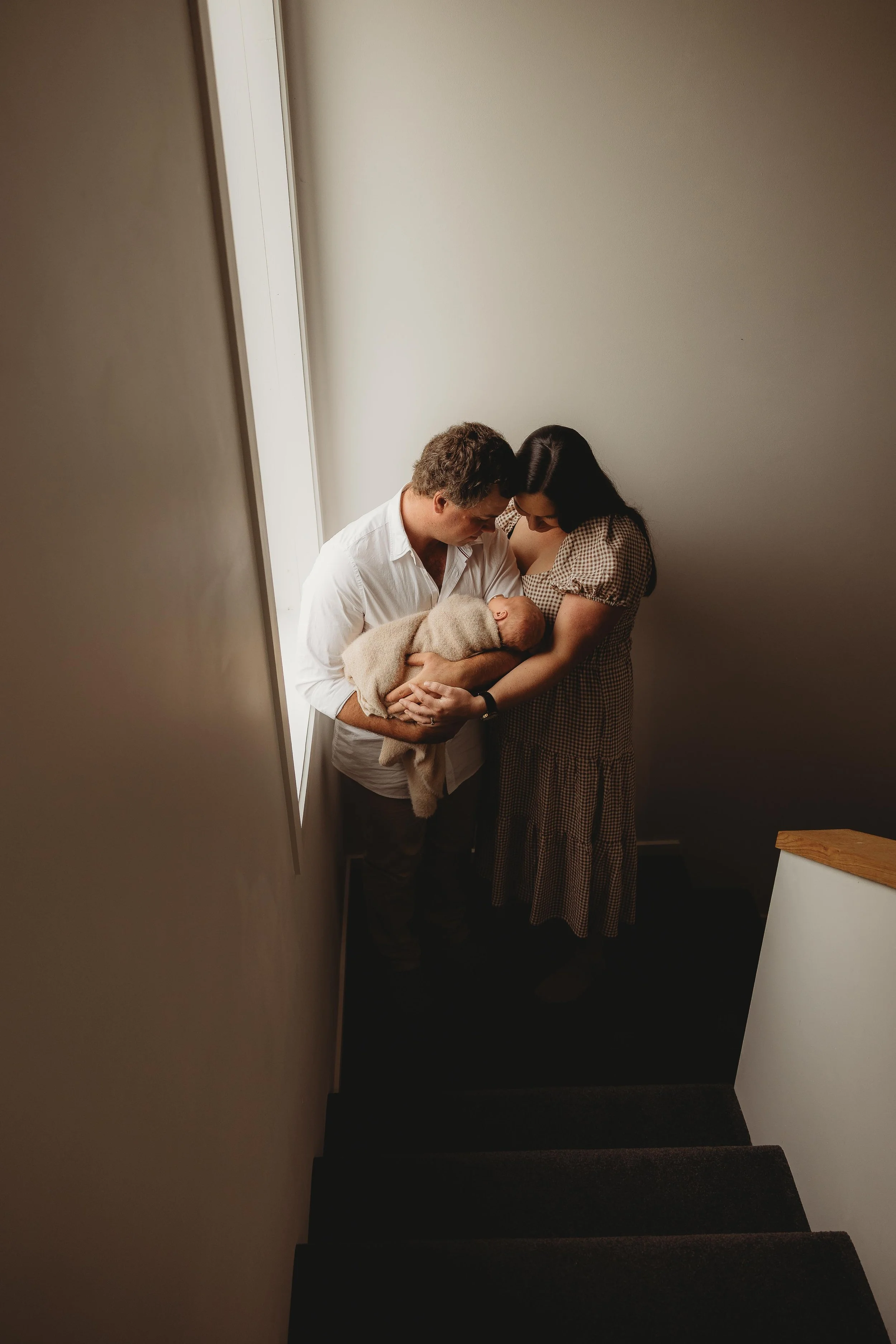 parents with newborn at home snuggled near window