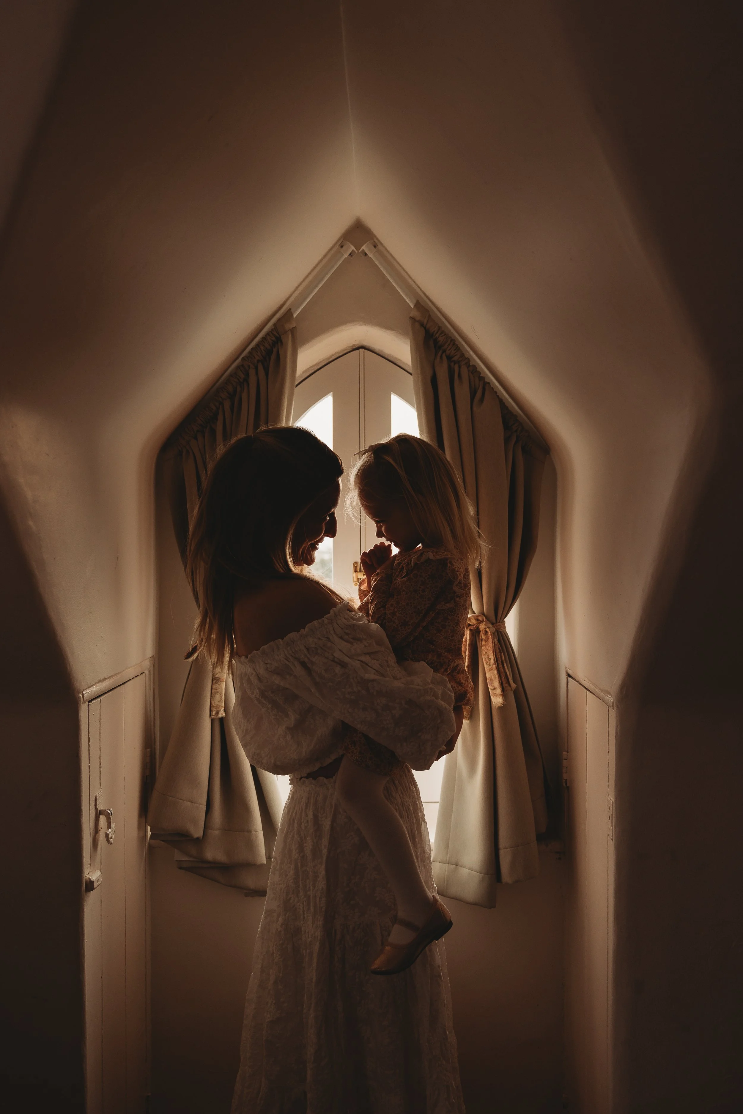 Mother and Daughter hugging together infant of window shilouet