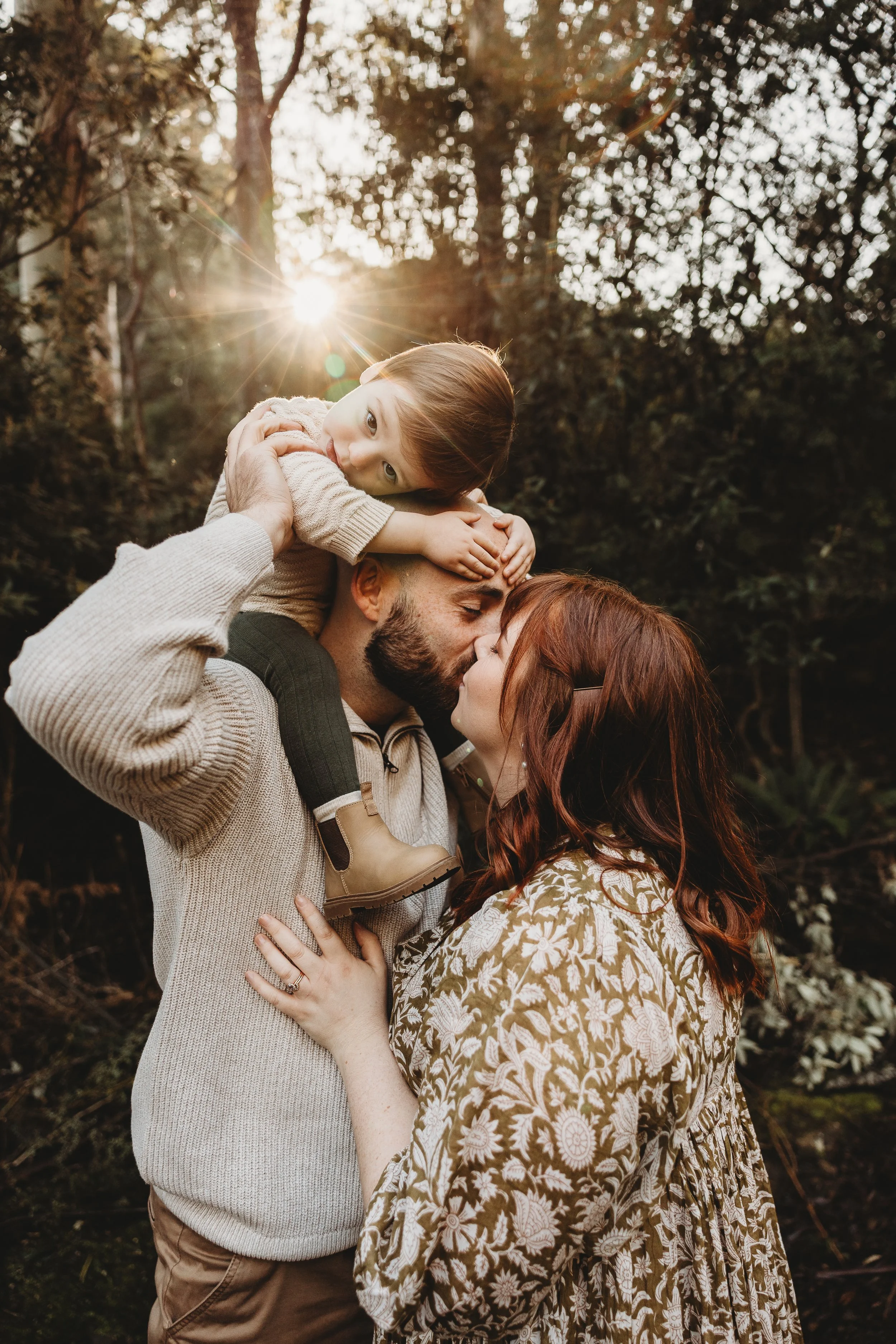parents in bush kissing with child on dads shoulder