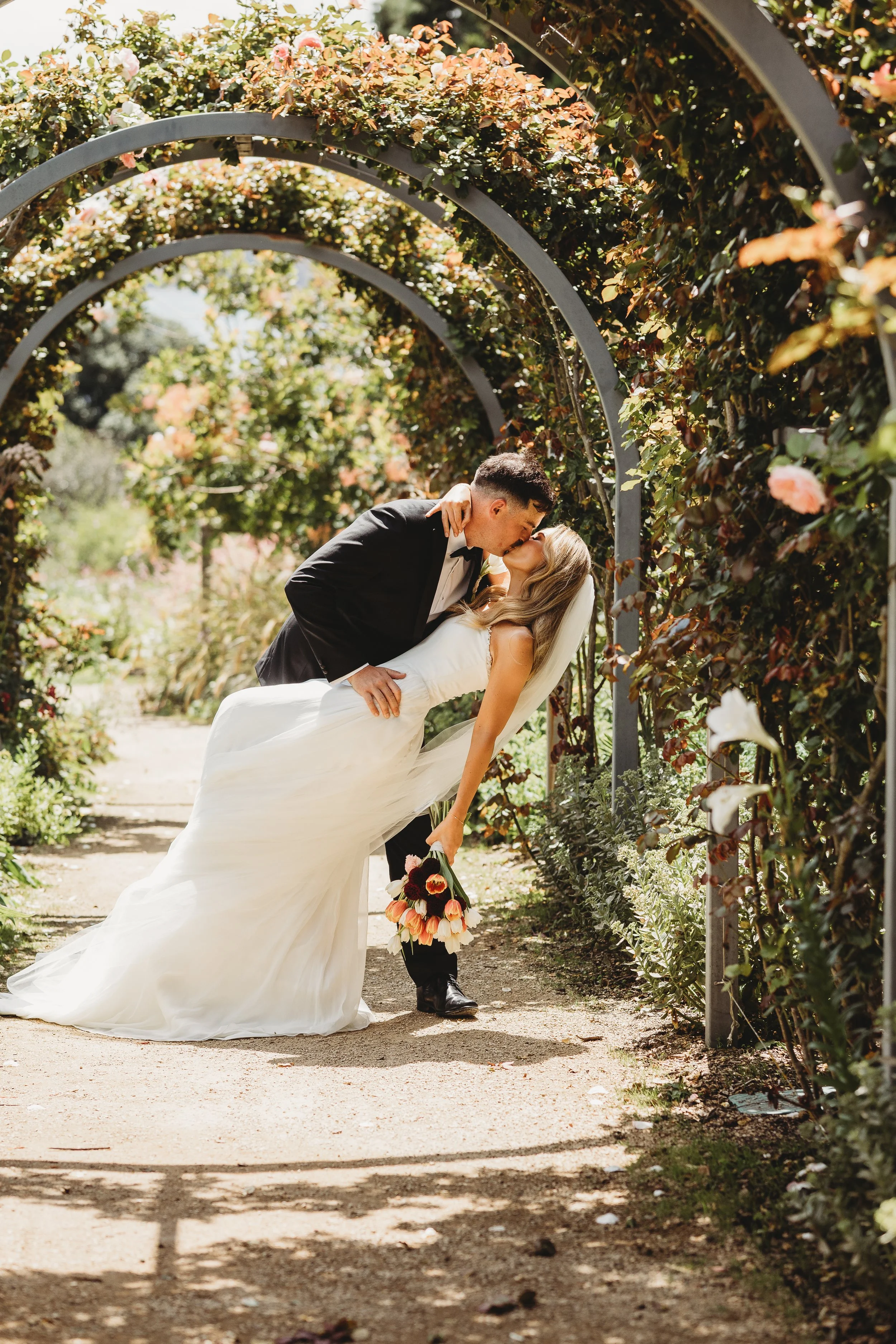 bride and groom doing a dip kiss in flower arches