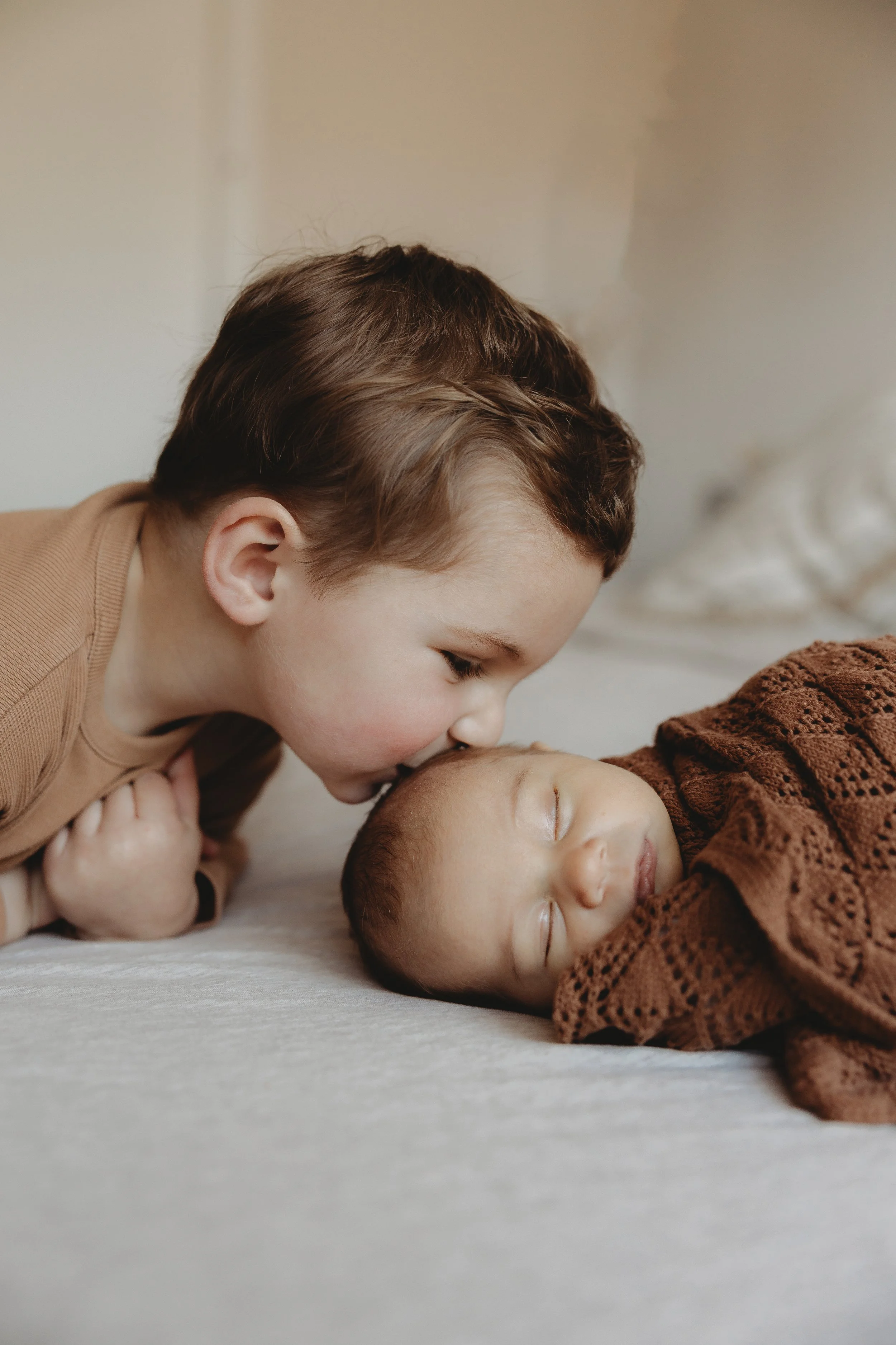 newborn baby in a basket ad big brother leaning over and giving baby a kiss