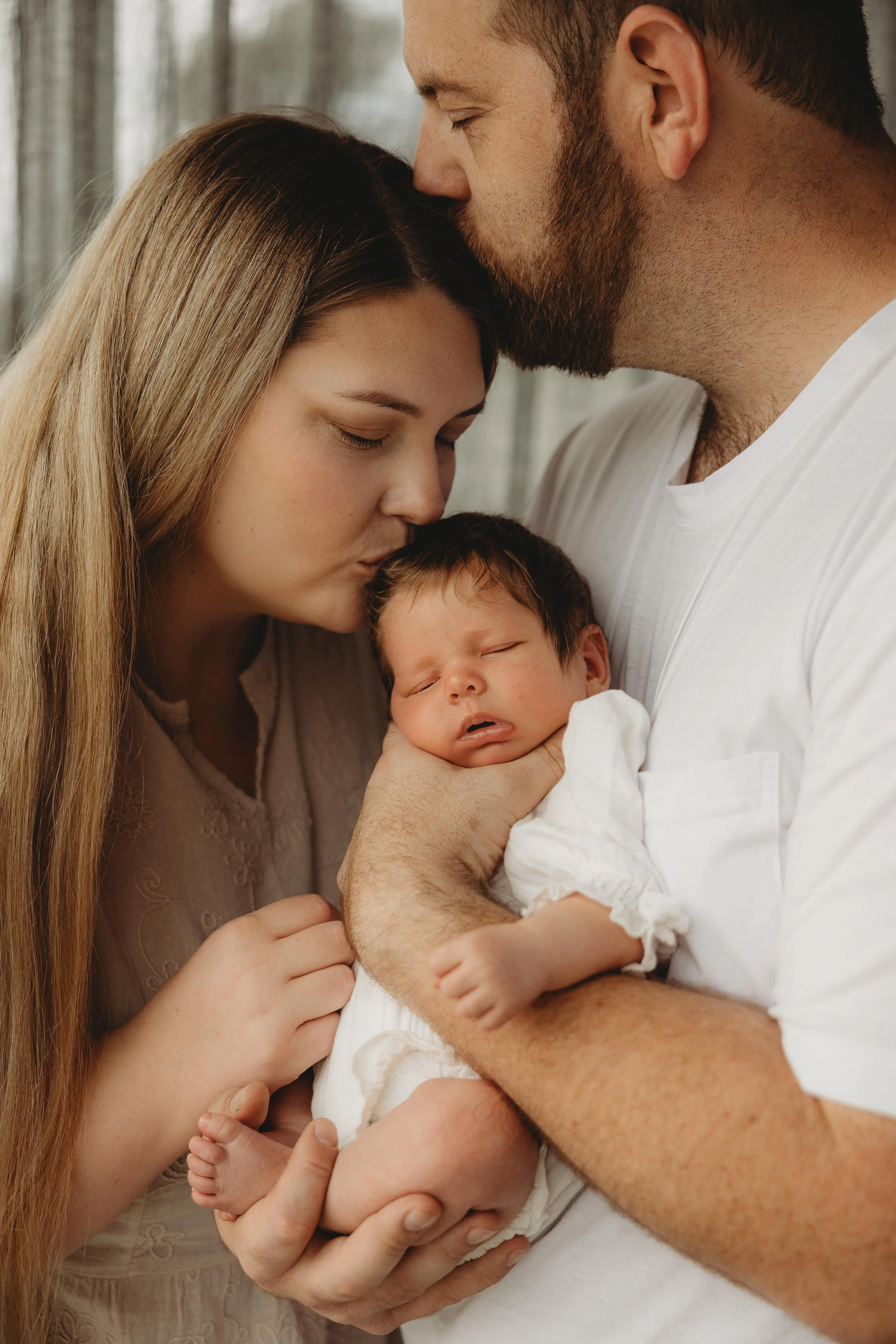 newborn baby cradle in dads arm with mum leaning in for snuggles