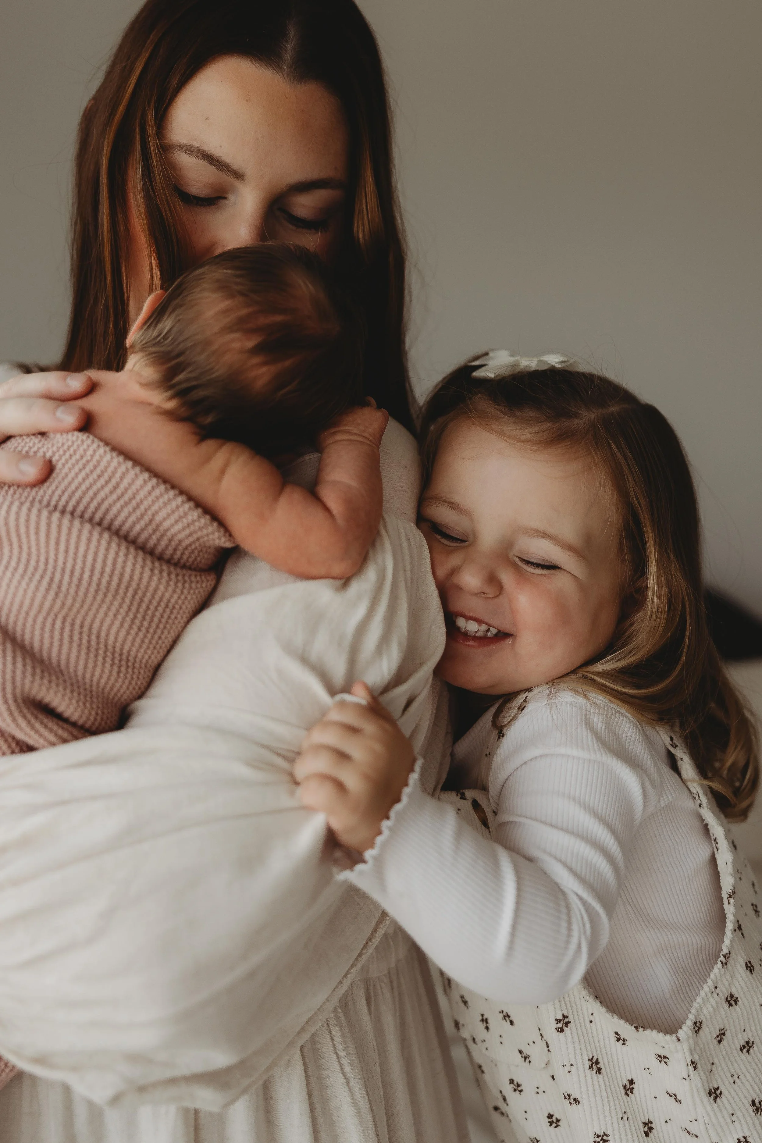 mum with newborn baby and little sitter hugging them both