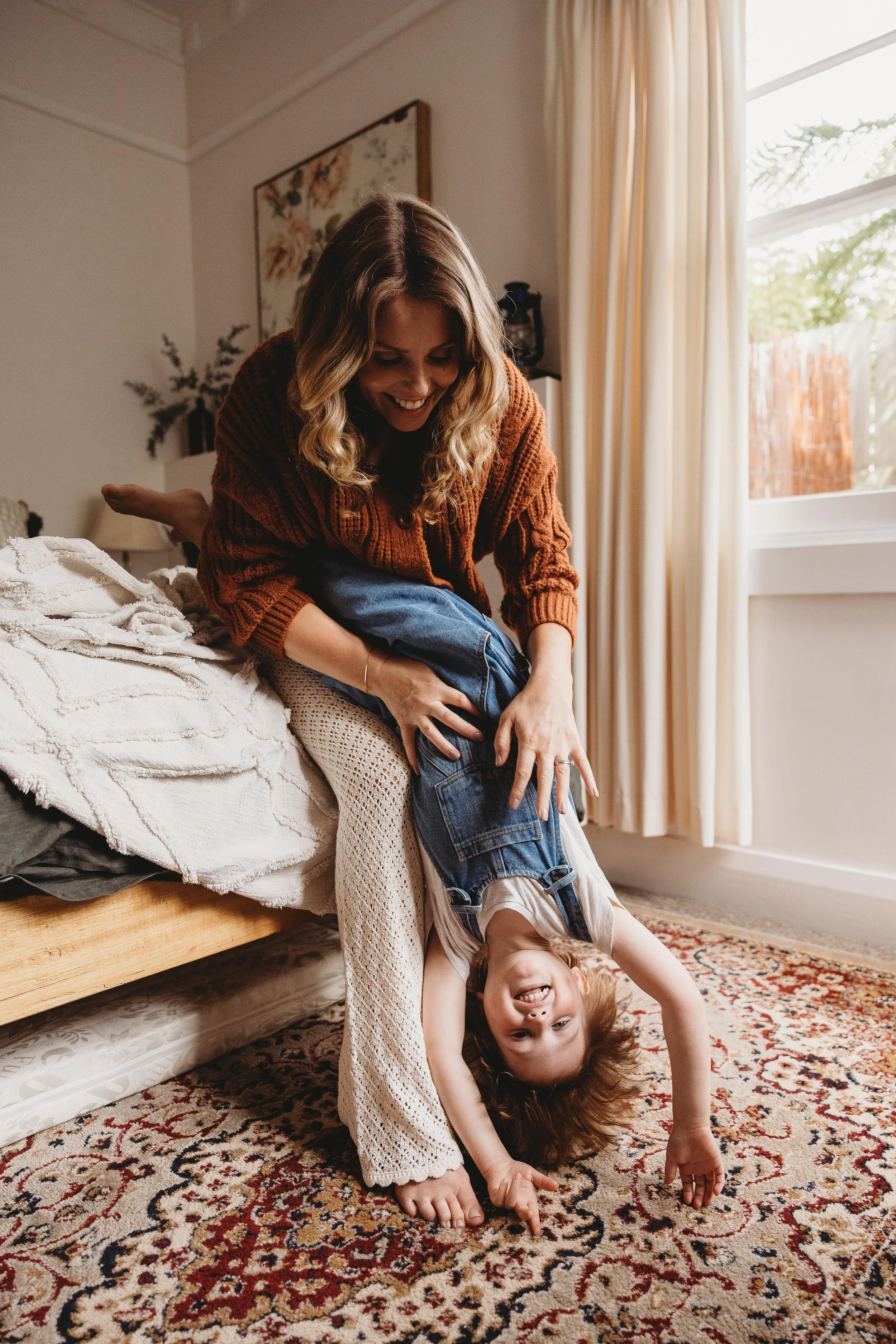 mum and son sitting on bed with child upside down being tickled