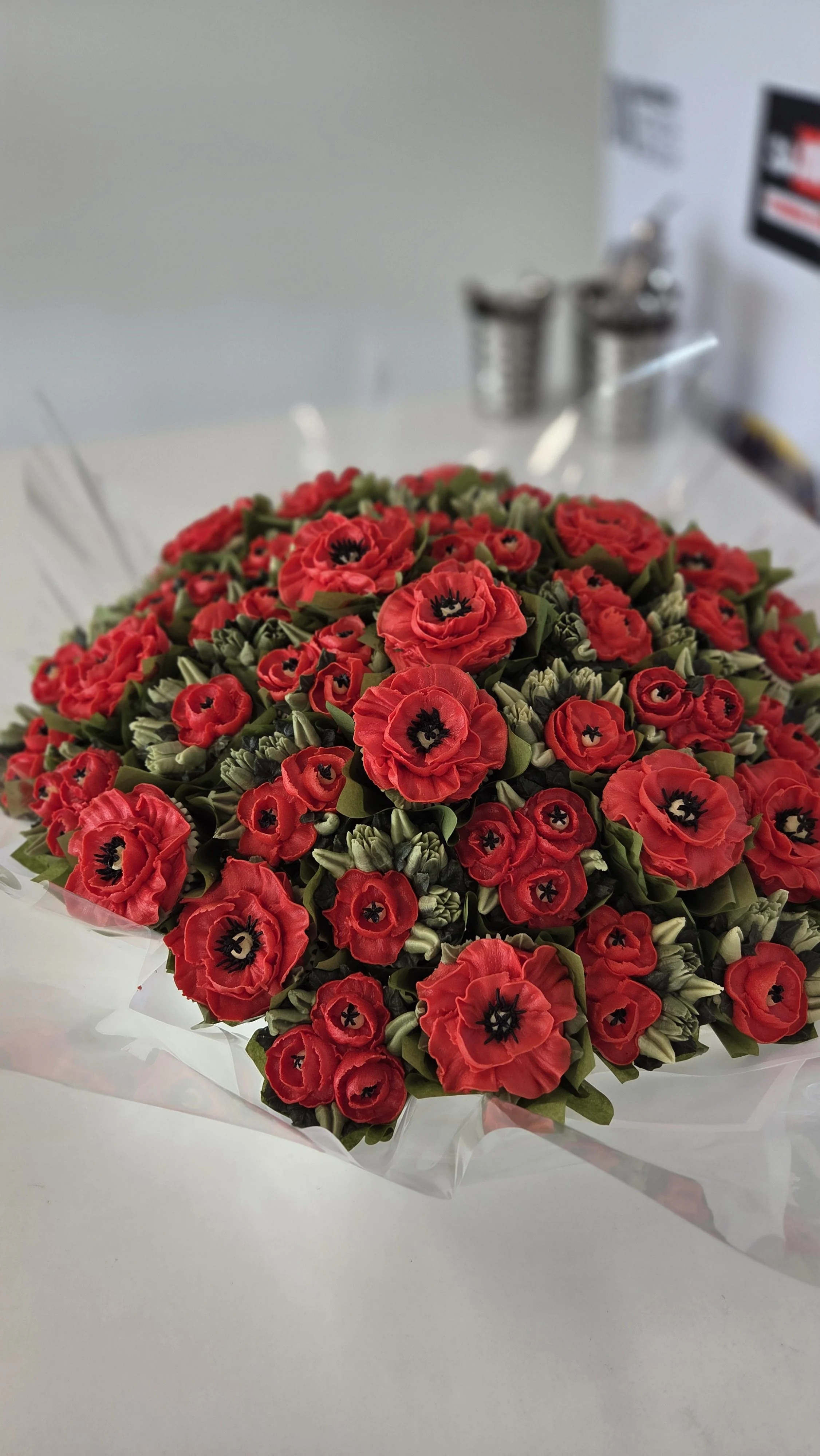 A cupcake bouquet of red poppies with green leaves.