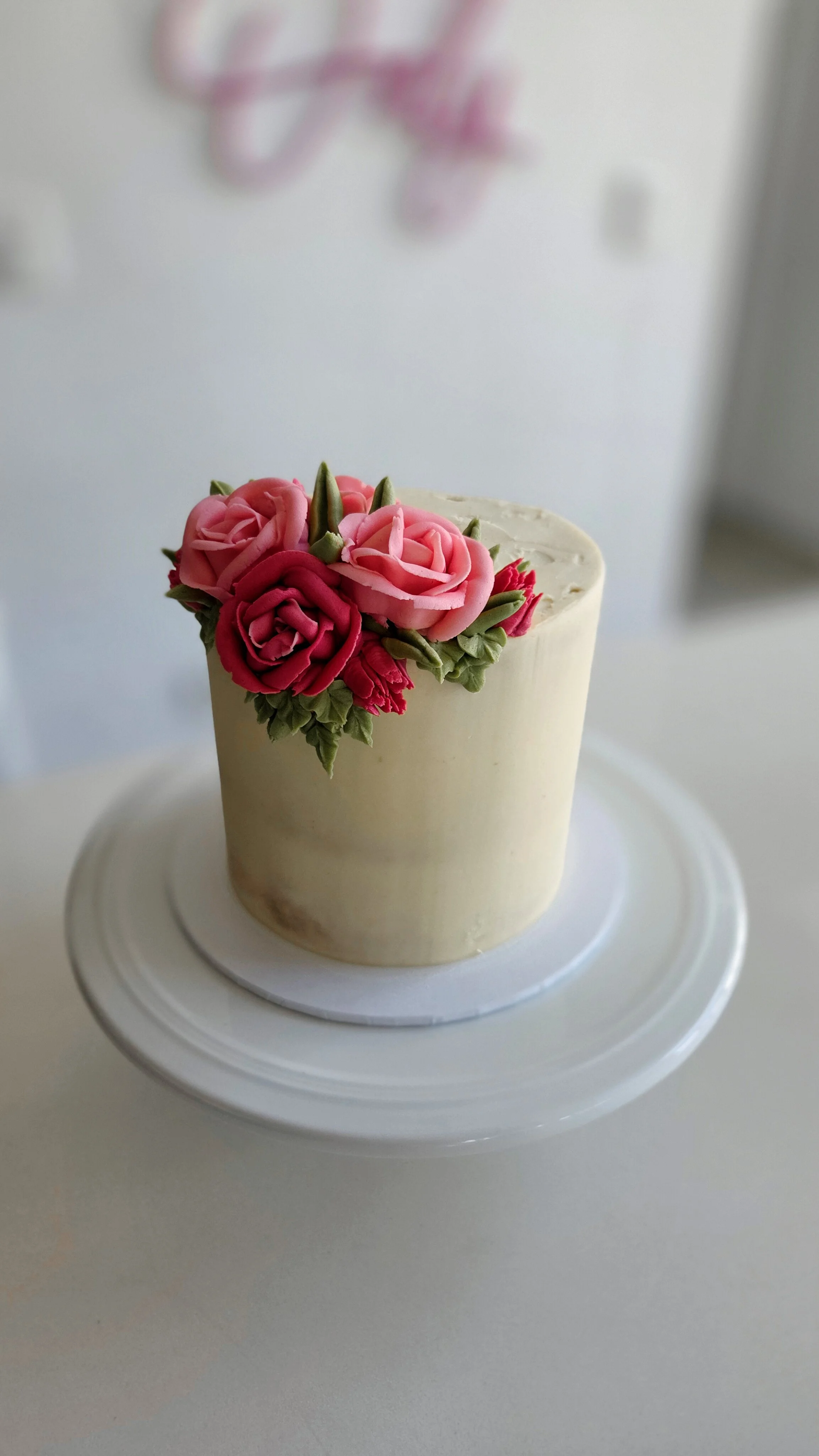 A small white cake decorated with pink and red buttercream roses on top, displayed on a white cake stand.
