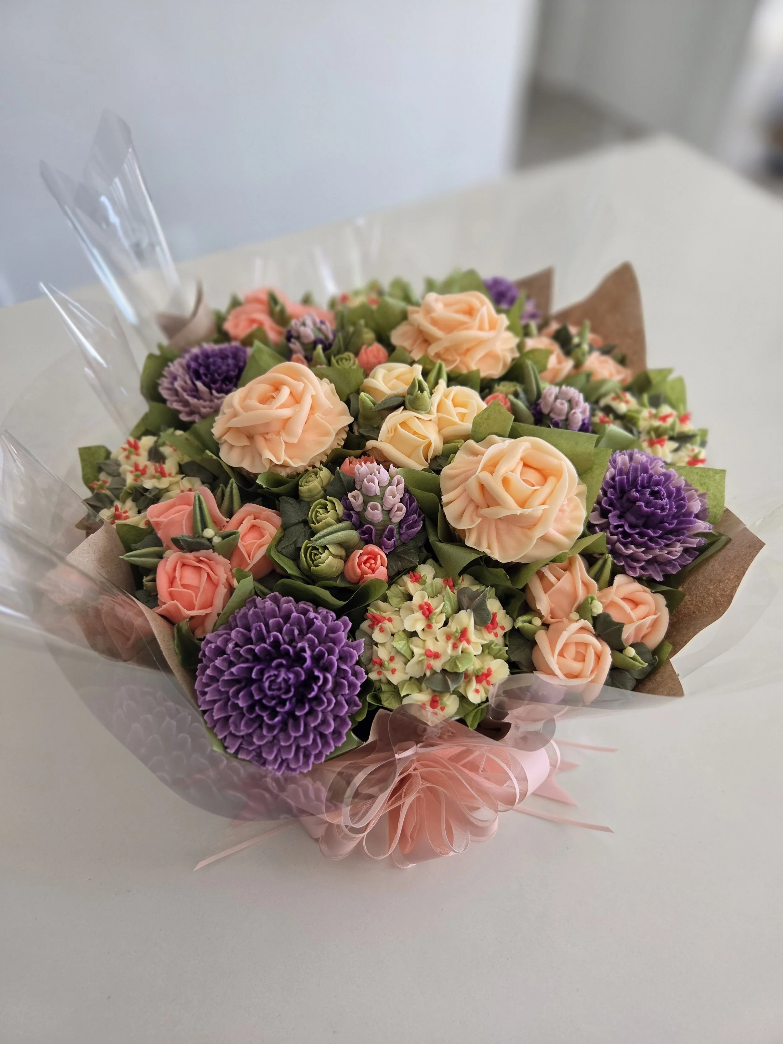 Bouquet of peach, purple, and pink flowers wrapped in pink and clear wrapping paper.