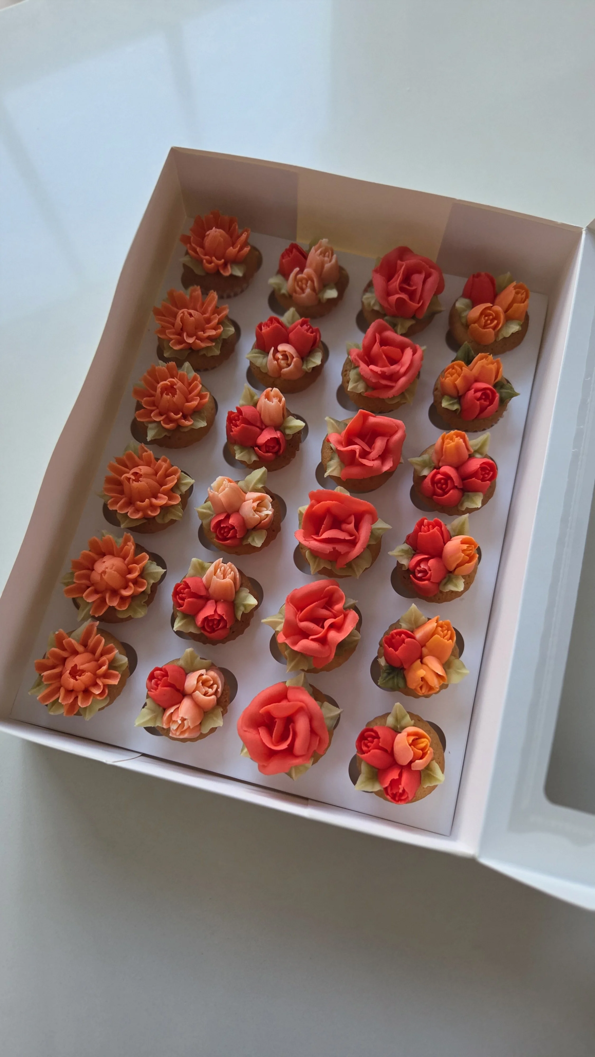 Box of decorated cookies with floral designs in orange, red, and pink colors.