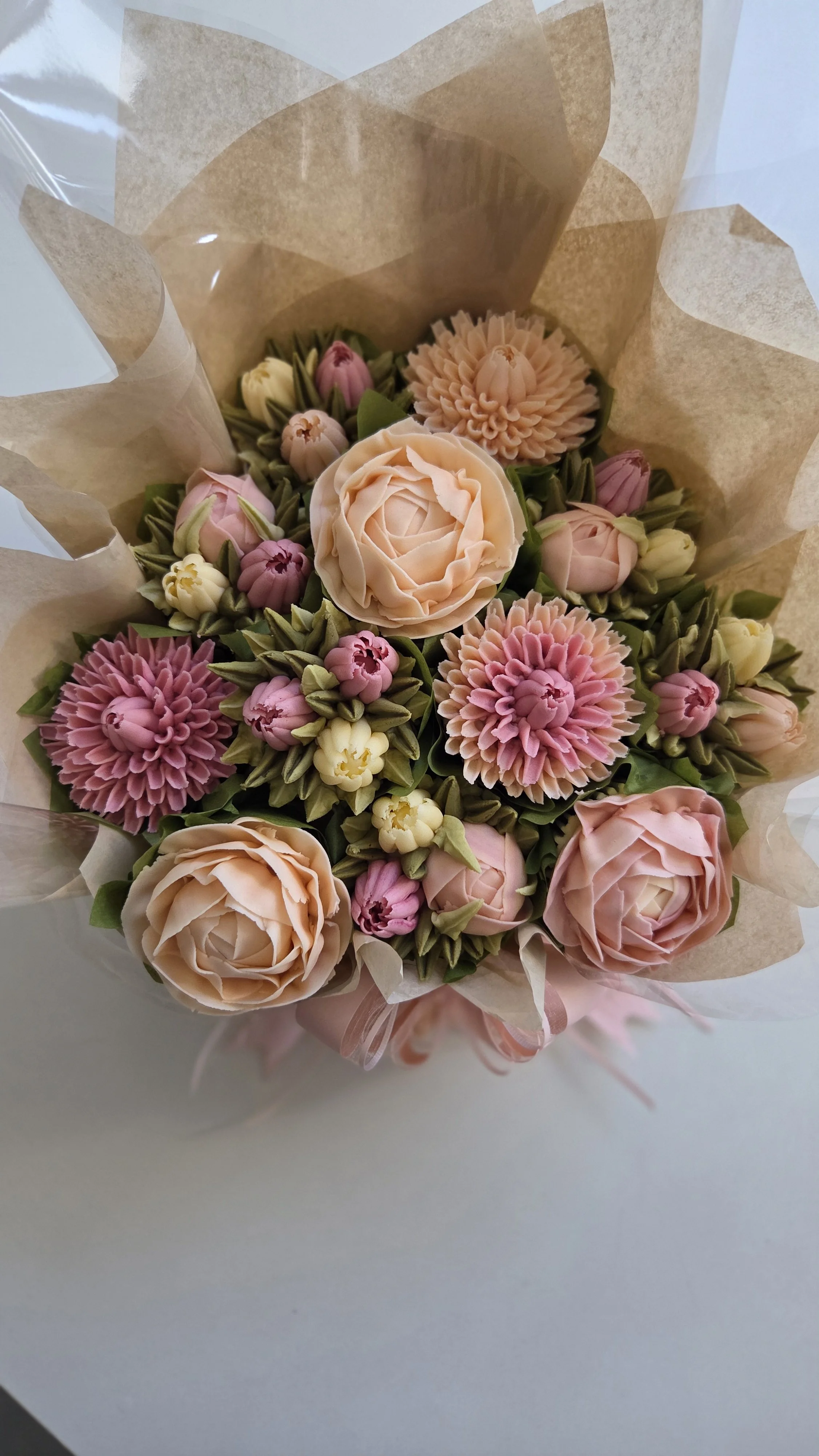 A bouquet of pastel-colored flowers including roses, daisies, and small buds wrapped in beige tissue paper.
