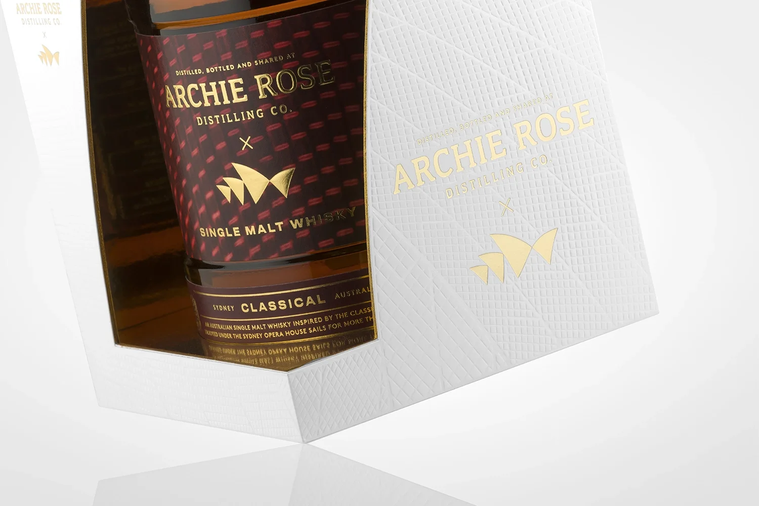 A bottle of Archie Rose single malt whisky in a white textured box with gold lettering and logo.