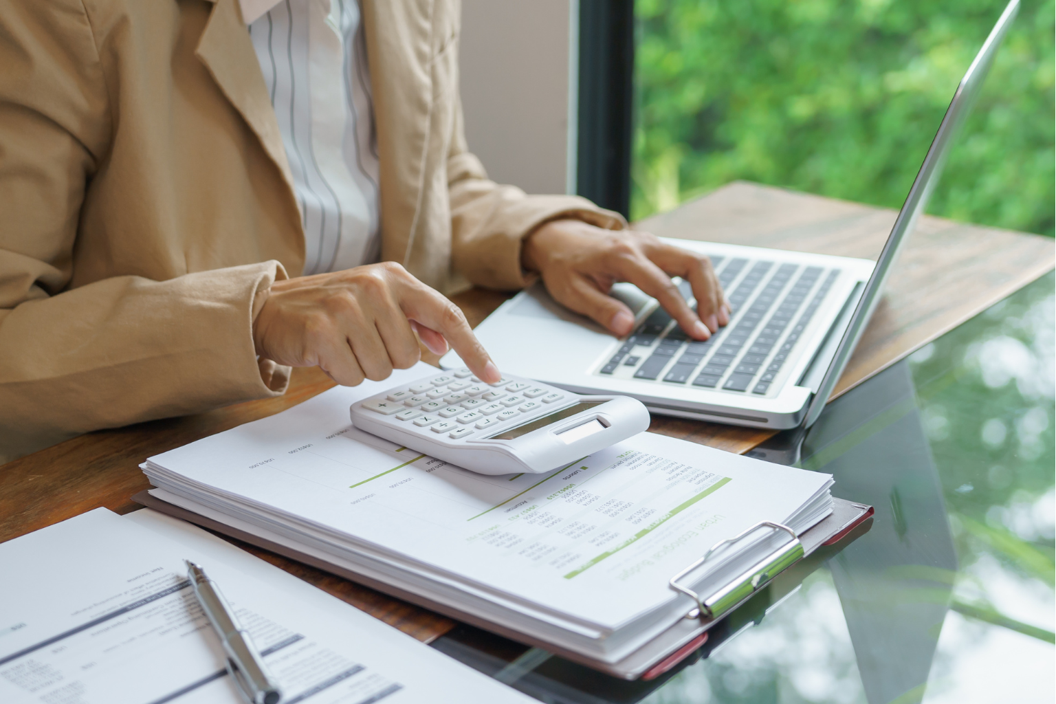 Person using a calculator and a laptop on a desk with financial documents.
