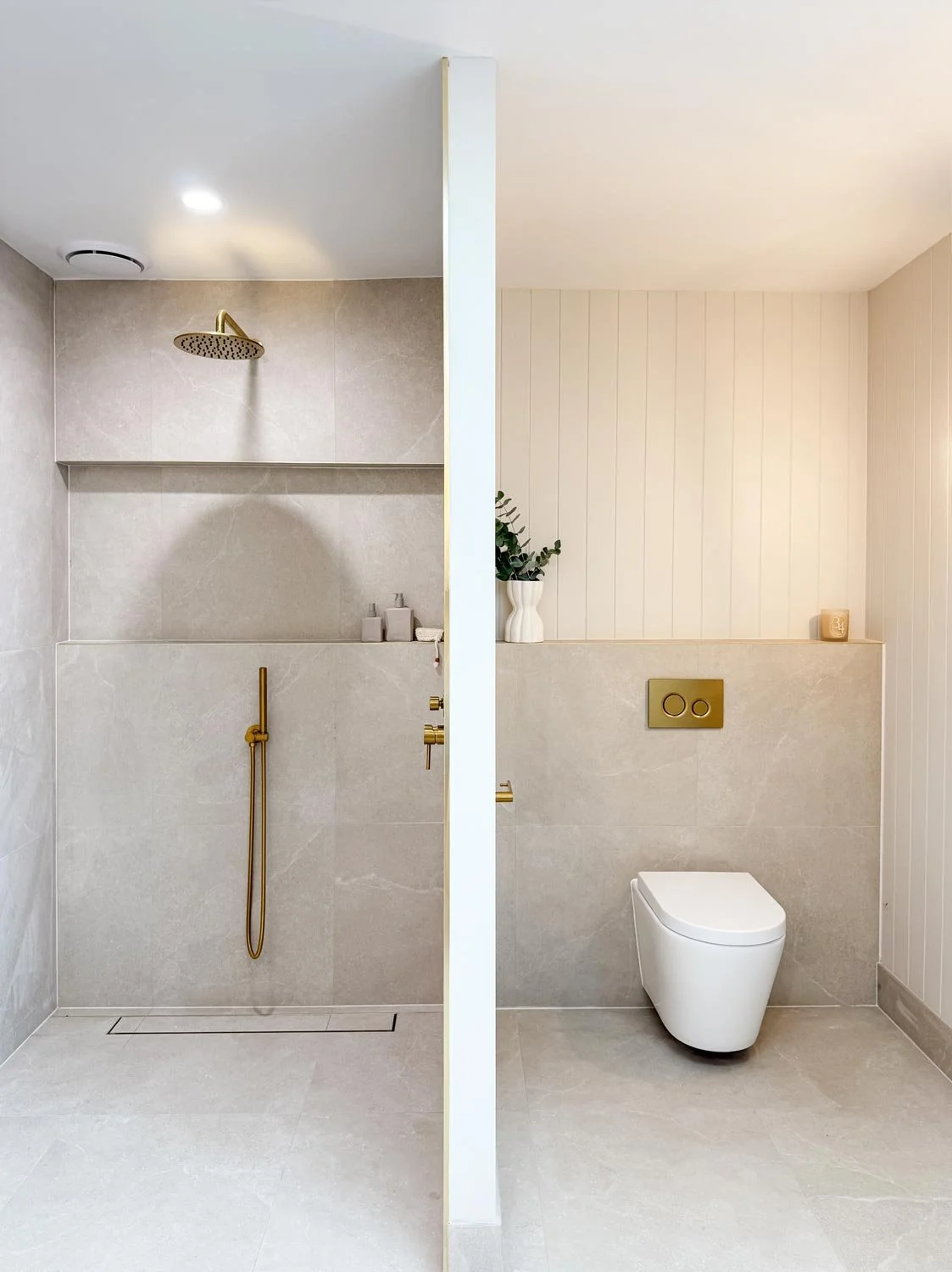 A side-by-side view of a modern bathroom showing a walk-in shower on the left, and a toilet on the right, with a partition in the middle.