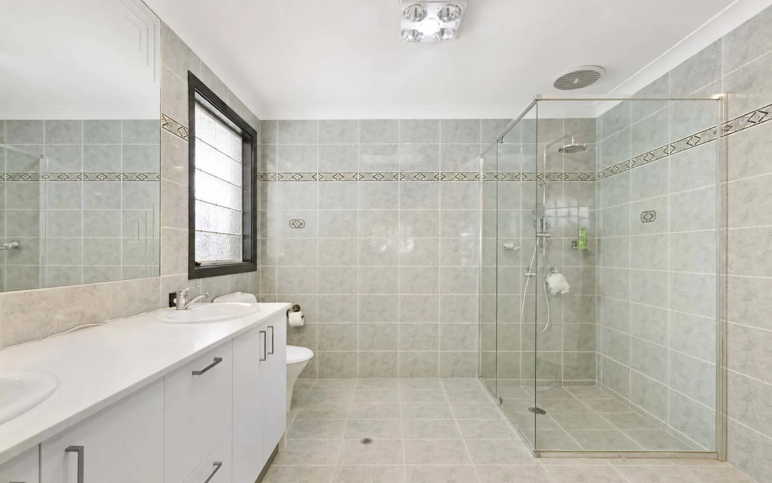Bathroom before renovation with old fittings and dated design, double vanity, shower and toilet shown.
