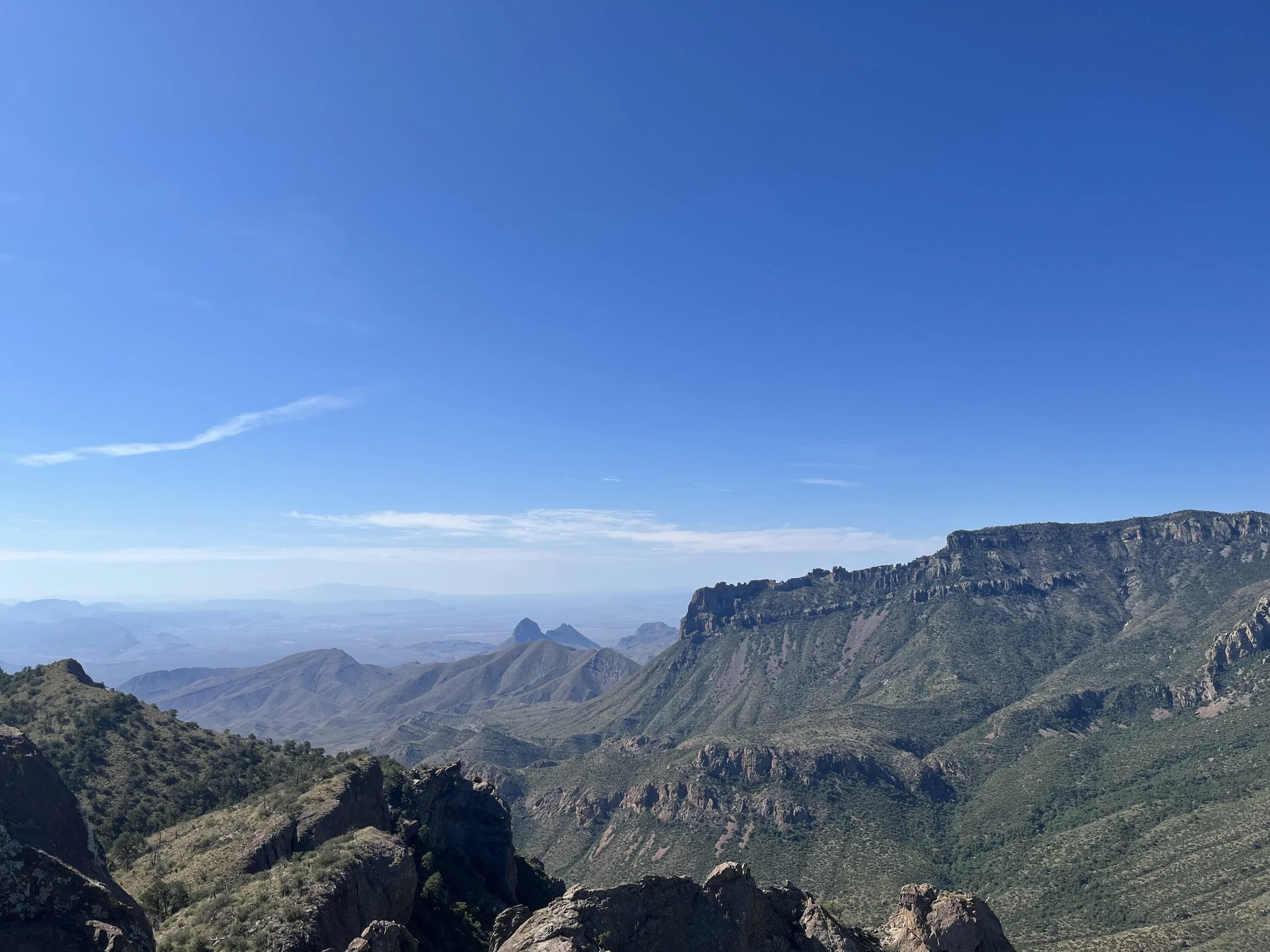 A panoramic view of mountain ranges under a clear blue sky with some clouds.