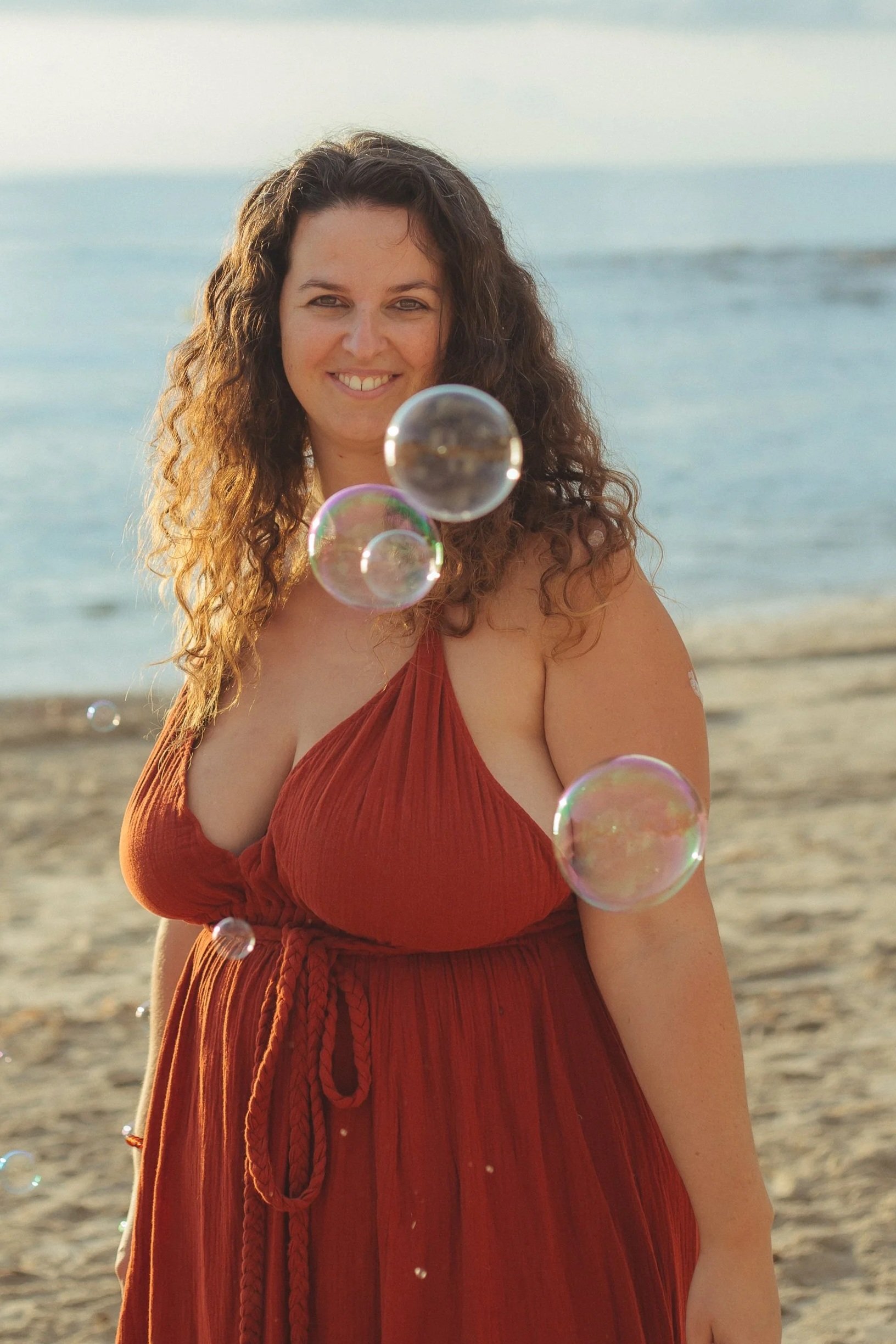 Maartje Wammes, zakelijk strateeg en business architect, staat lachend op het strand in een terracotta jurk met zeepbellen om haar heen — zelfverzekerd, grounded en aanwezig