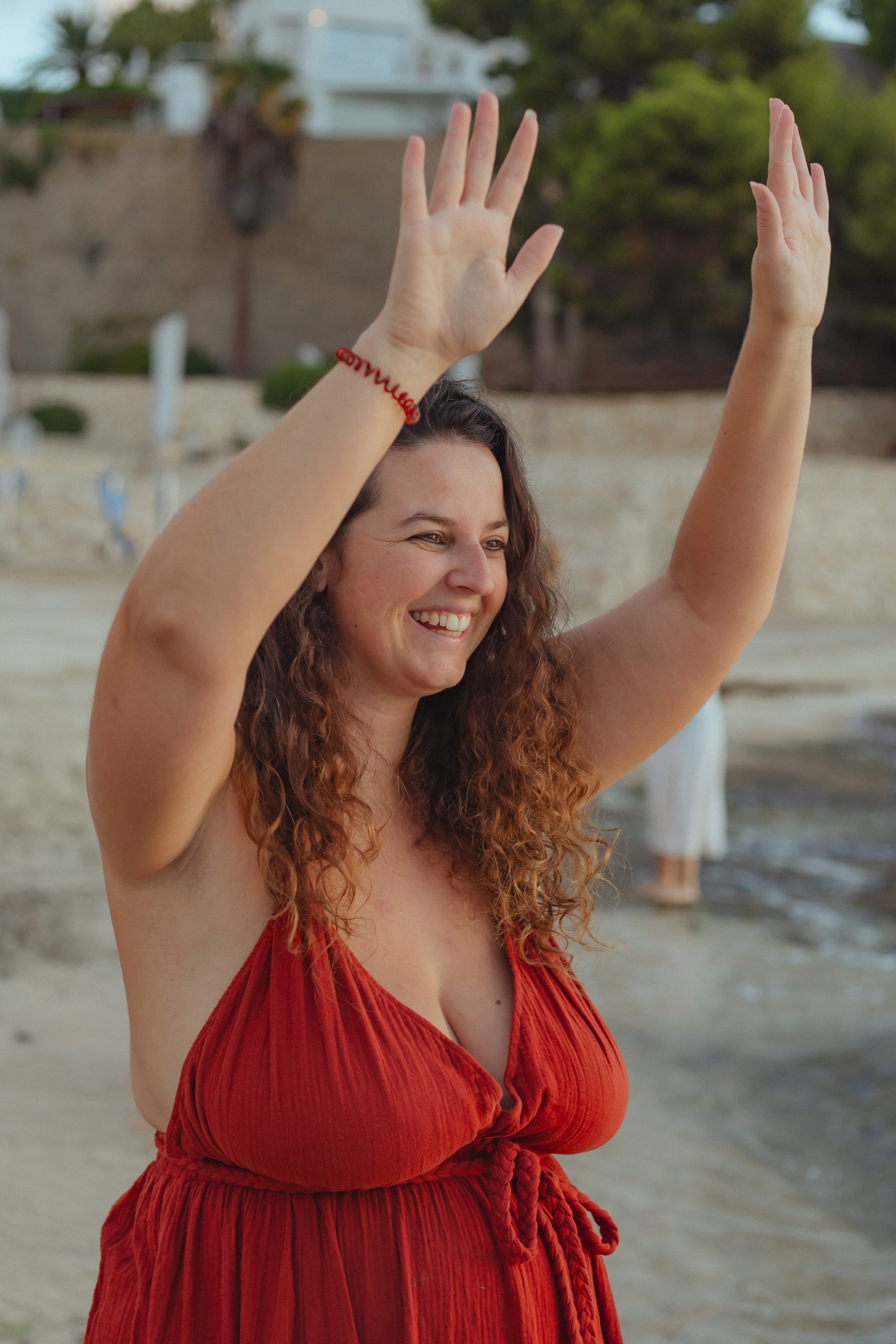 "Portret van Maartje Wammes op het strand met opgeheven armen en een glimlach tijdens een inspirerende bijeenkomst."