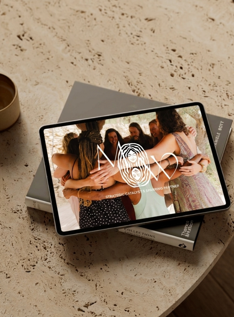 A tablet displaying a group of women hugging, with a logo and the words "Strategic Catalyst & Supporting Partner" on the screen, resting on two books on a textured table.