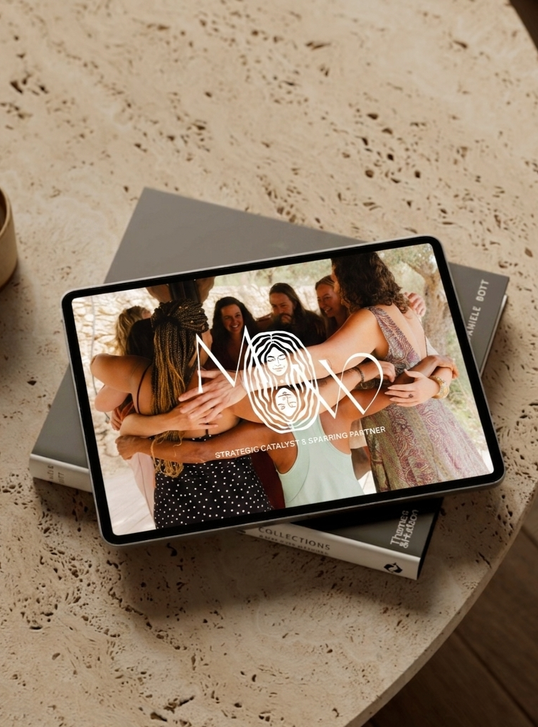 Tablet met de website van Maartje Wammes op een travertin salontafel, met een afbeelding van een groep mensen die elkaar omhelst tijdens een strategische bijeenkomst.