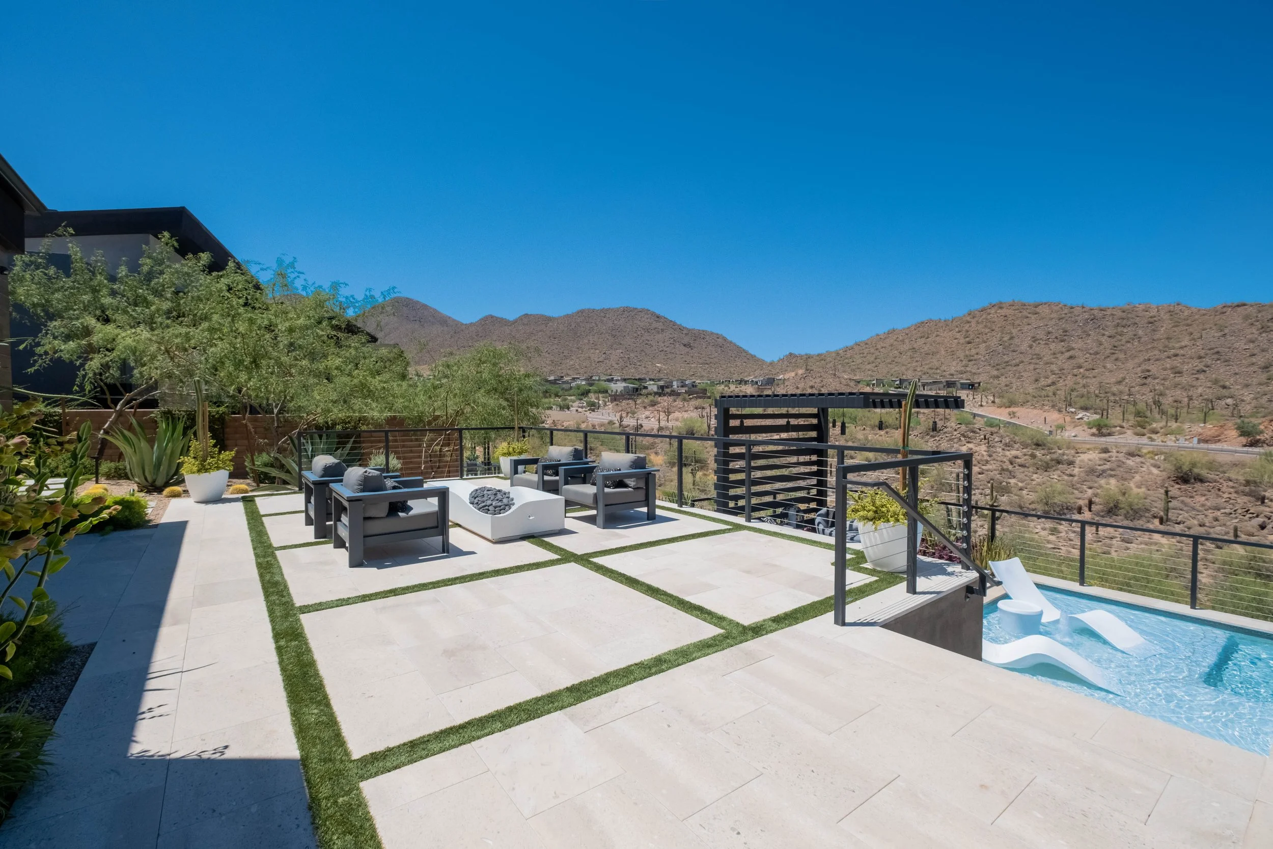 A backyard patio area with outdoor seating, potted plants, and a view of desert mountains under a clear blue sky.