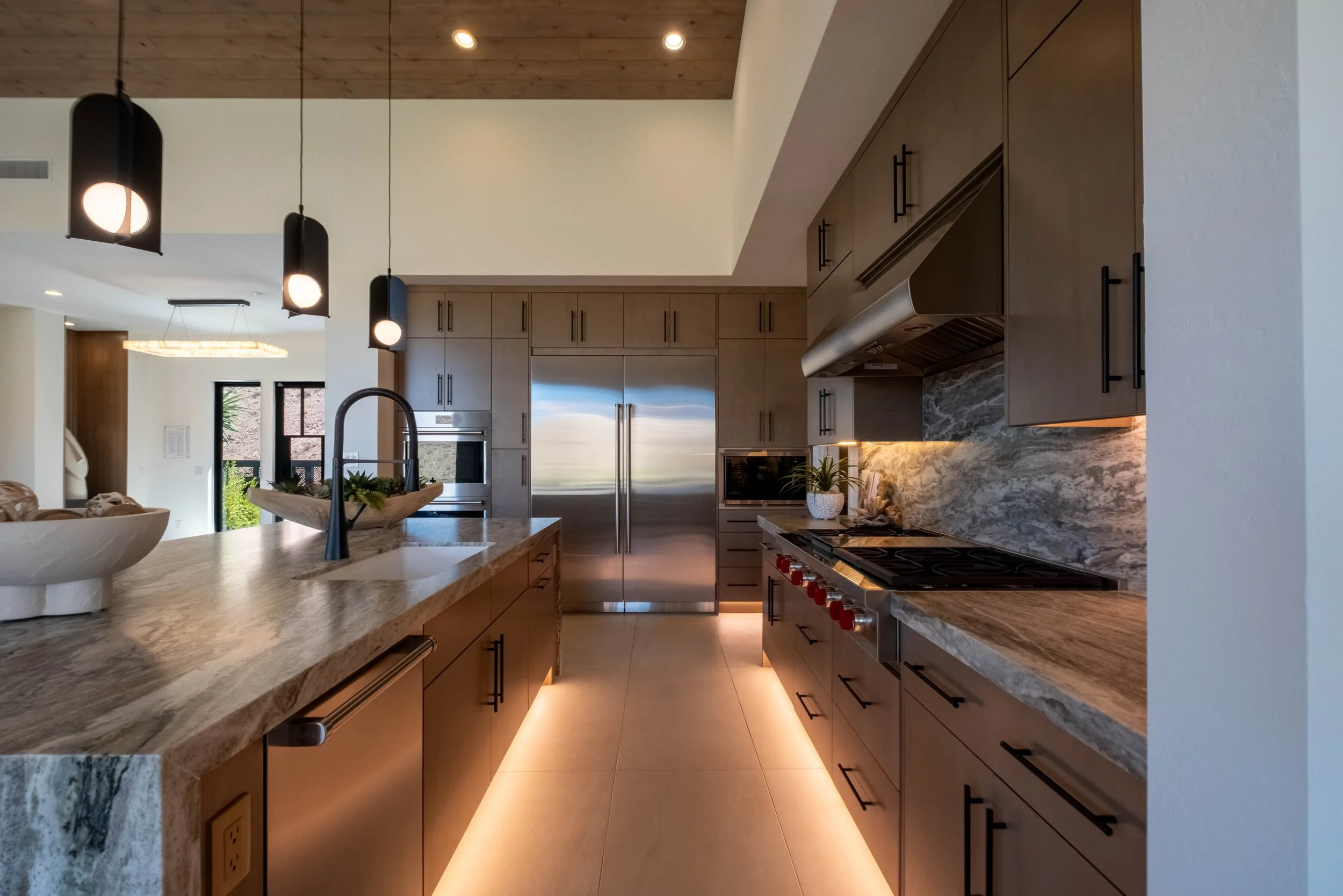 Modern kitchen with wooden cabinets, granite countertops, stainless steel refrigerator, and black pendant lights hanging from a wooden ceiling.