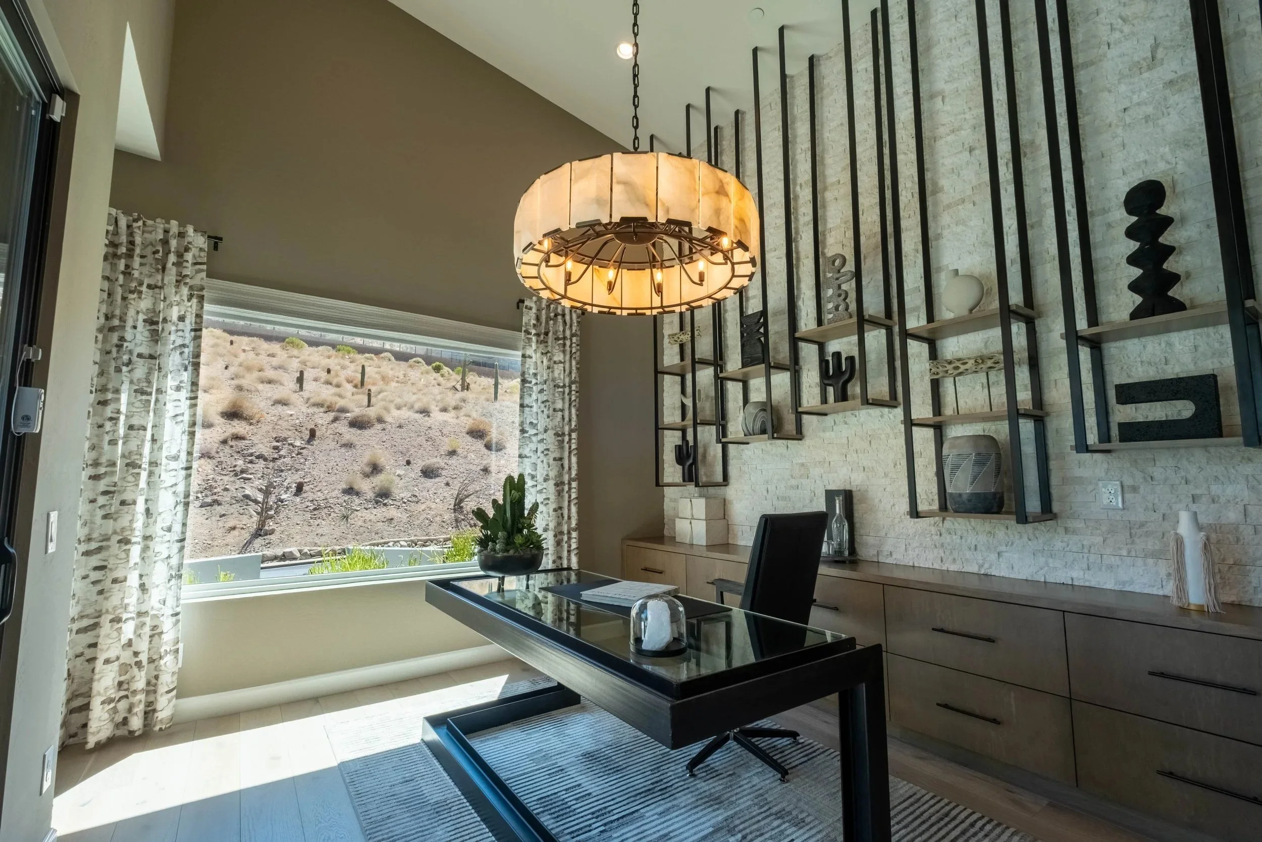 Modern dining room with large window showing desert landscape, contemporary chandelier, open shelving with decorative objects, and table set for a meal.