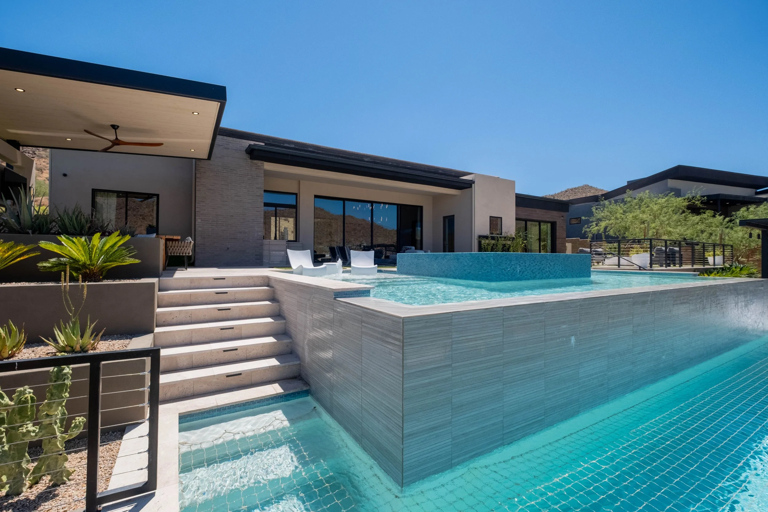 Modern house with an outdoor pool under a clear blue sky, surrounded by desert landscape and greenery.