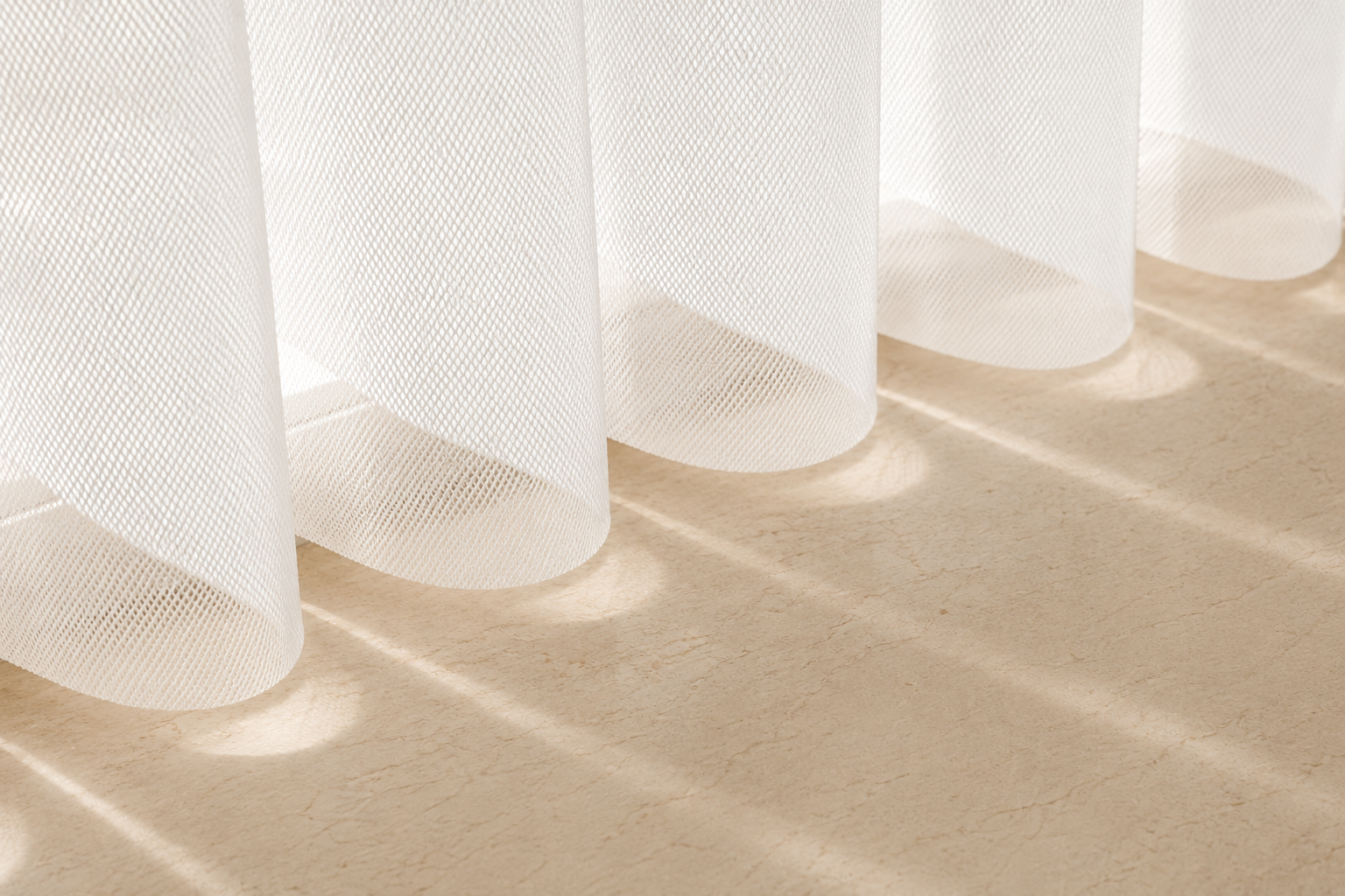 Close-up of white sheer curtains with sunlight casting shadows on a beige marble floor.