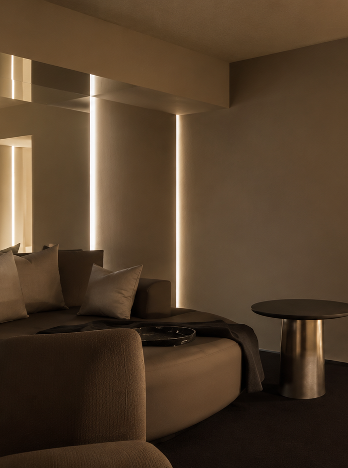 Salon moderne avec canapés beiges, coussins, table noire, lumière indirecte